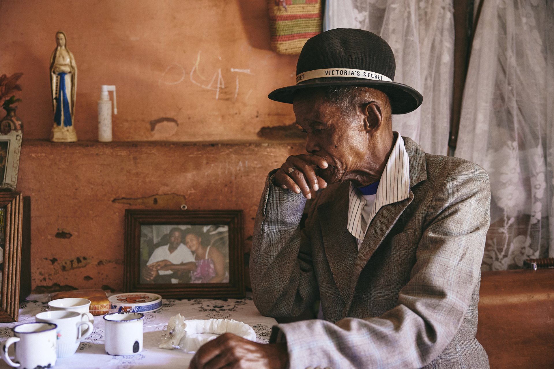 Dada Paul sits at home, in Antananarivo, Madagascar, beside a framed photograph of himself and his wife, who has passed away. He often forgets about her death and confuses his daughter, Fara, for his wife.