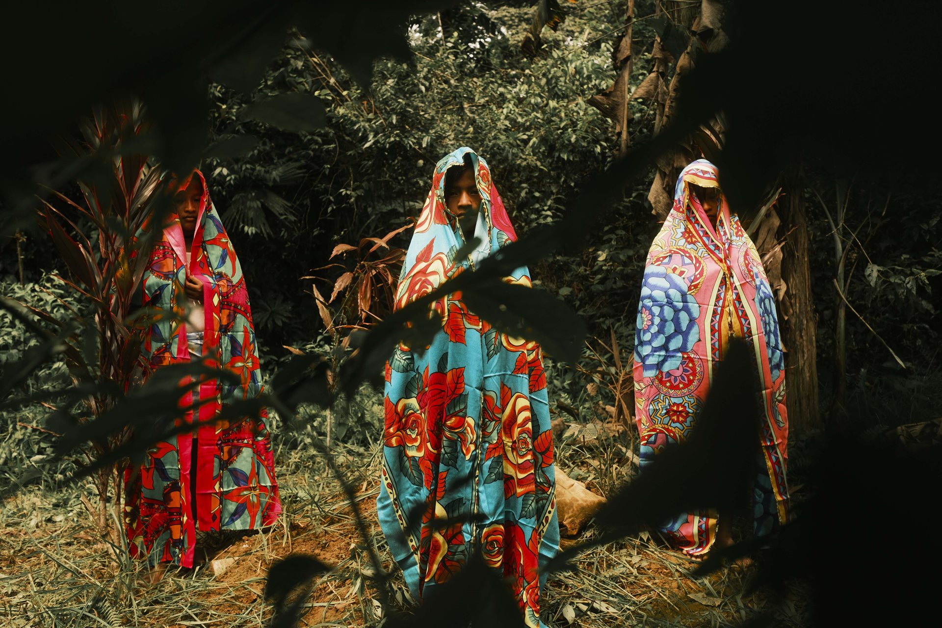 María Camila, Luisa, and Noraisi Birry stand by the grave of their sister, Yadira, while wearing the paramus Yadira left behind. Yadira Birry (16) took her own life with a paruma on 7 April 2023. Chocó, Colombia.