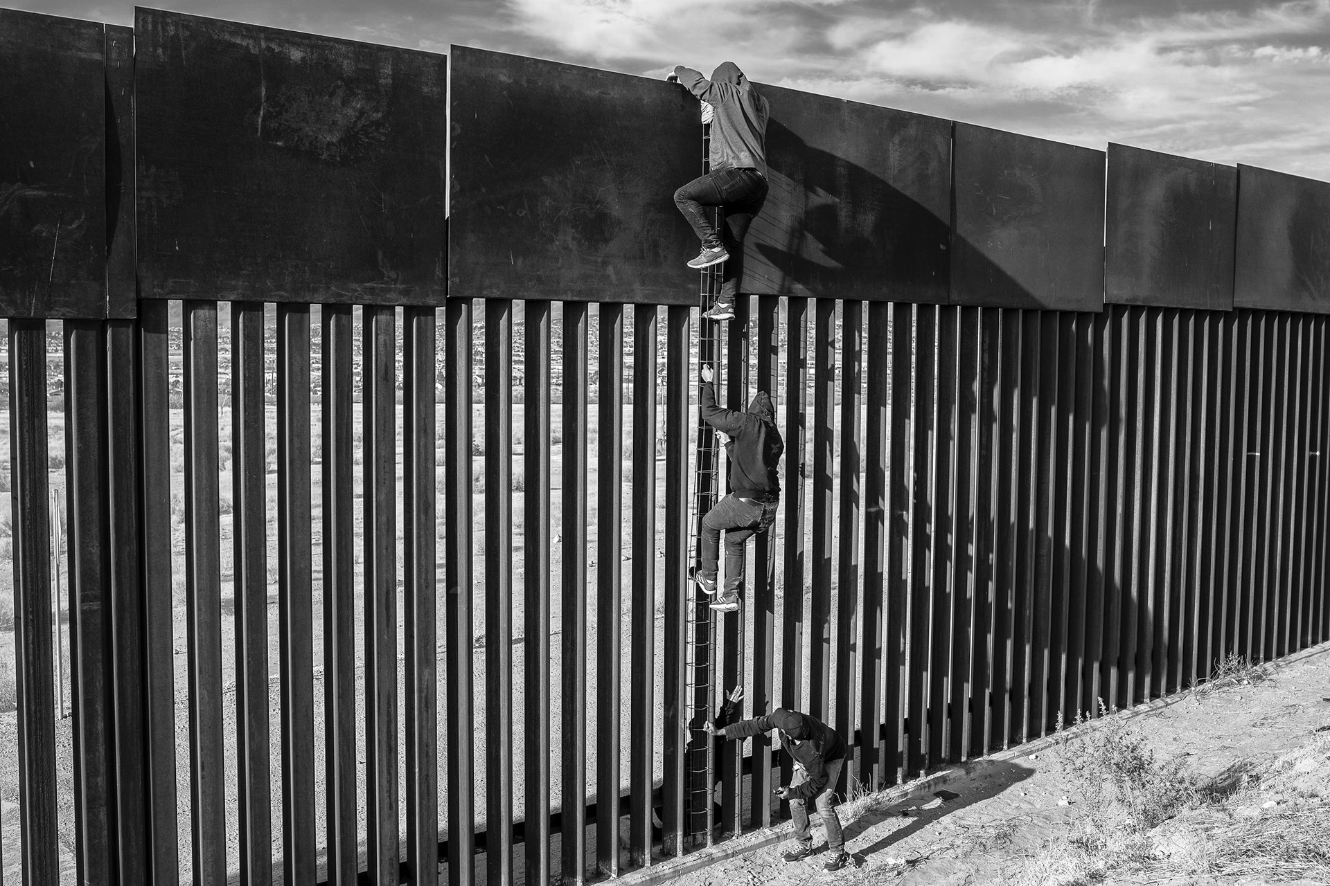 <p>Migrants use a homemade ladder to climb a section of the border wall with the help of a smuggler, in Ciudad Juárez, Mexico.</p>
