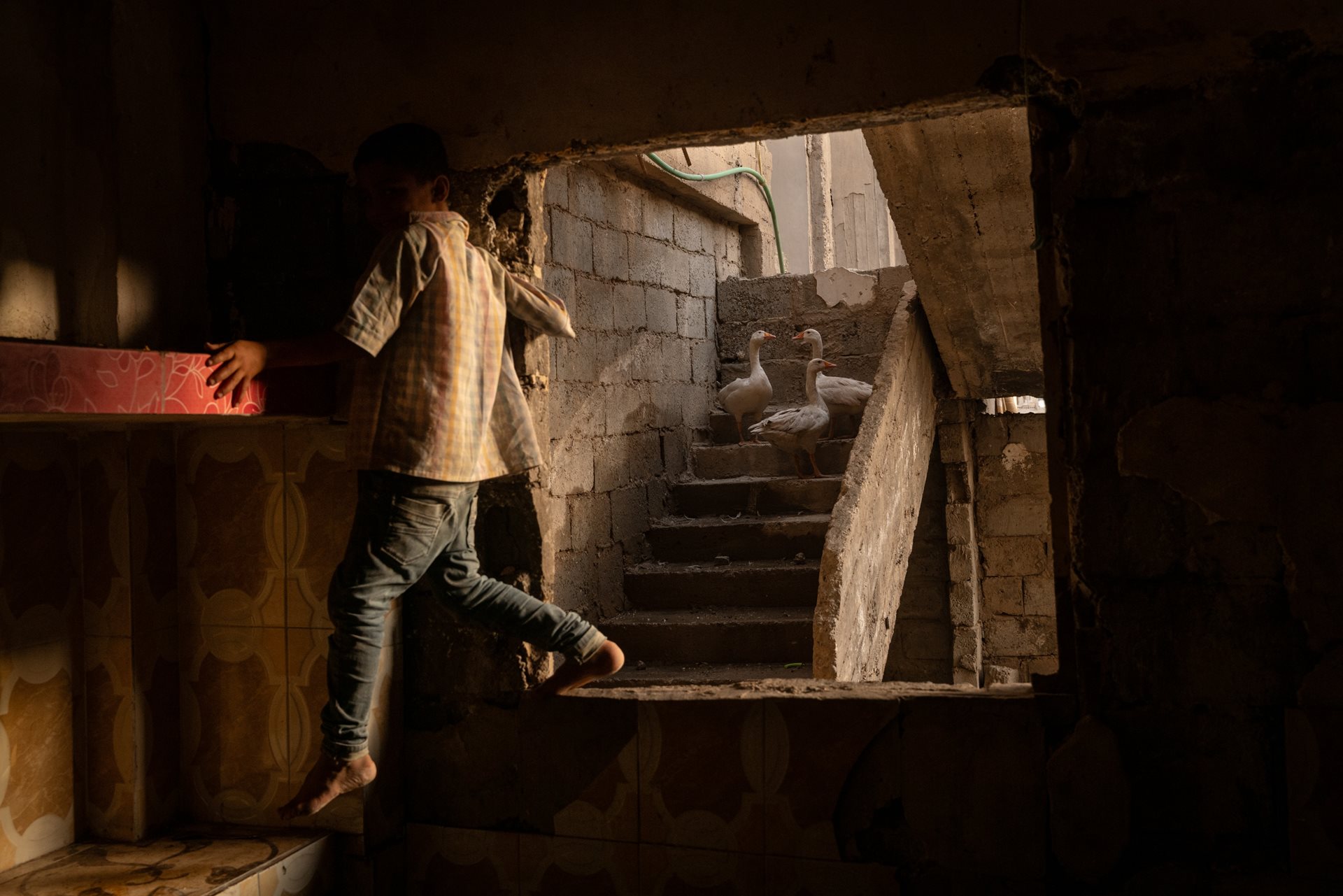 A son of Abdelatif Daham Al Hummada climbs through the kitchen window of the family&rsquo;s heavily damaged home, stripped of copper wiring, tiles, and fittings by looters.&nbsp;Deir al-Zour, Syria.<br />
&nbsp;