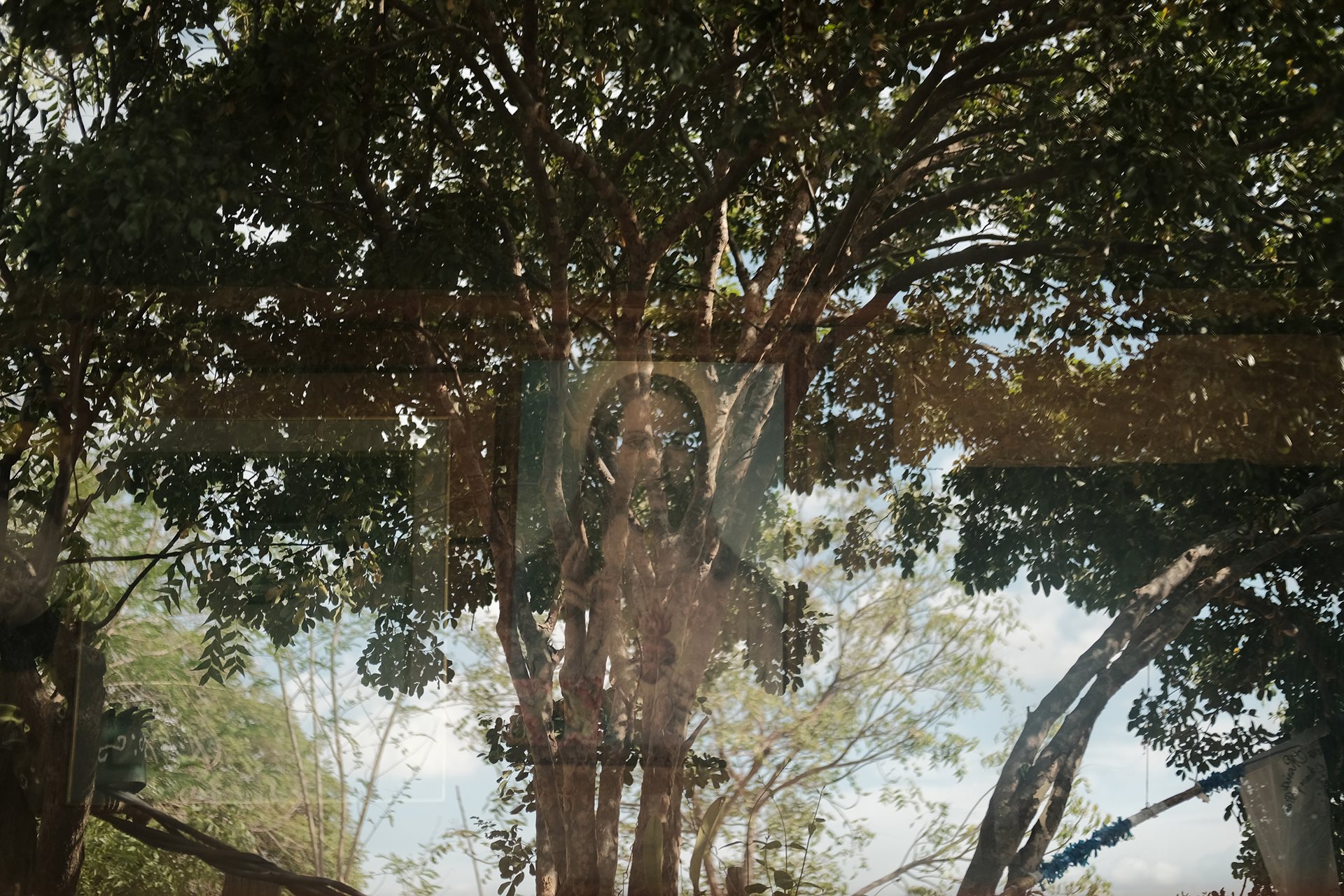 A painting of Jesus Christ is reflected by the window. Placed by the photographer&rsquo;s late grandfather, it is the sole male presence remaining inside his grandmother Orfelina&rsquo;s home in Los Patios, Norte de Santander, Colombia.