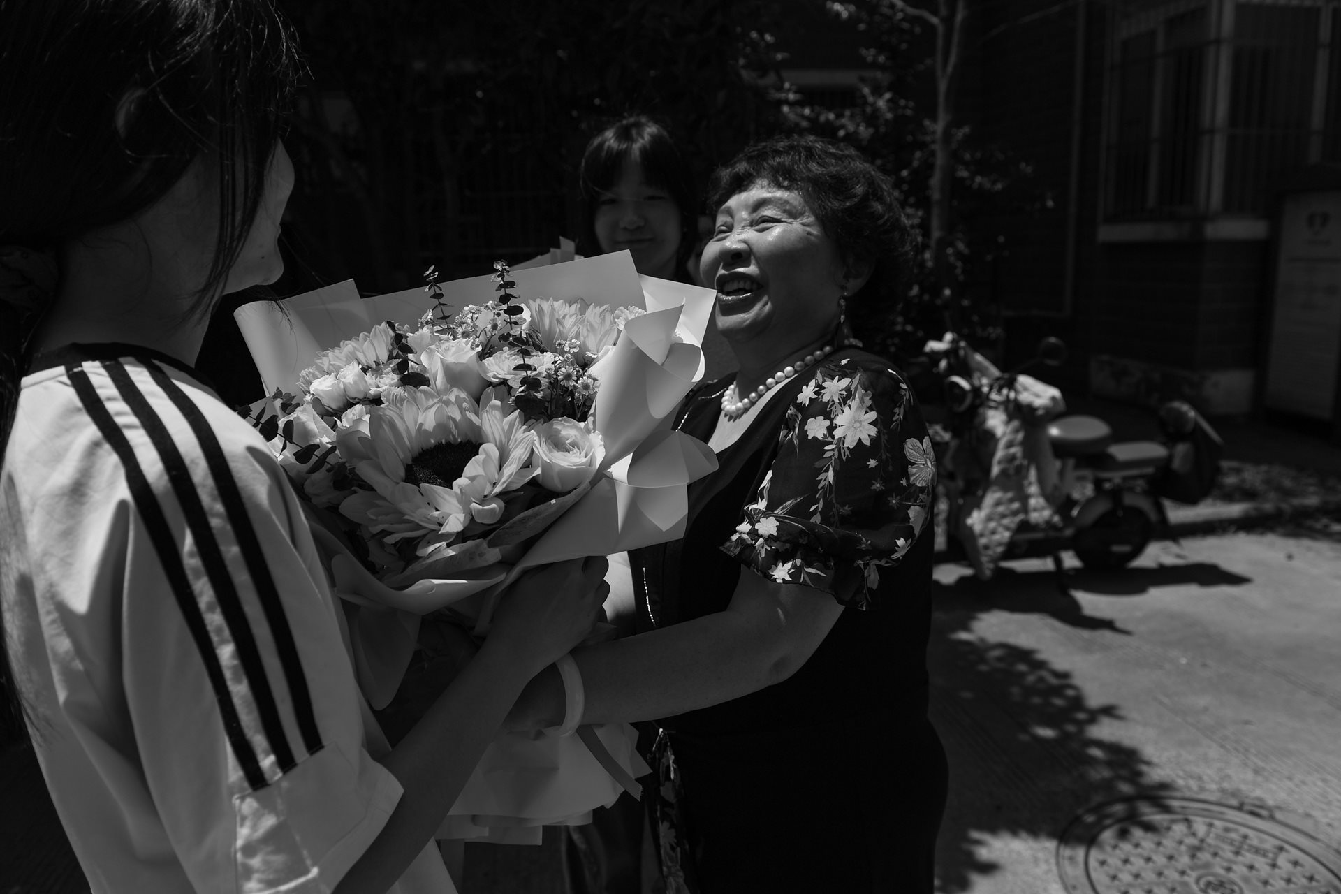 75-year-old Sheng Hailin presents her daughters with flowers after they complete their high school entrance exams. It is a personal milestone as well as a culminating moment for the 15-year project documenting a shīdú family's second chance at hope. Hefei, Anhui Province, China.
