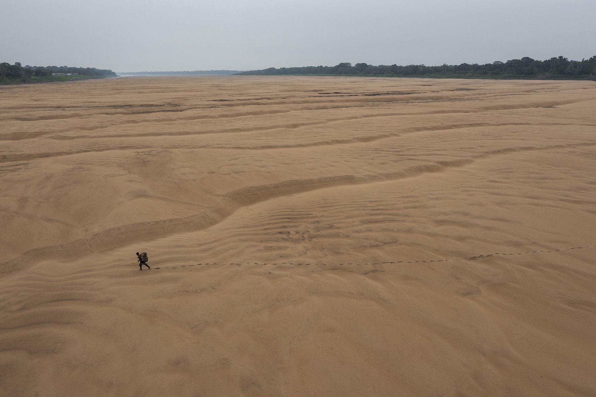 A fisherman walks across the dry bed of a branch of the Amazon River, near the Porto Praia Indigenous community. Tefé, Amazonas, Brazil.