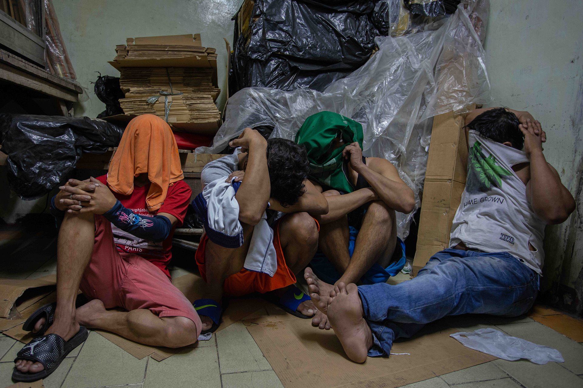 <p>Men shield their faces from the media after being arrested in a food factory that police claimed to be a drug den, in Pandacan, Manila, the Philippines. &nbsp;</p>
