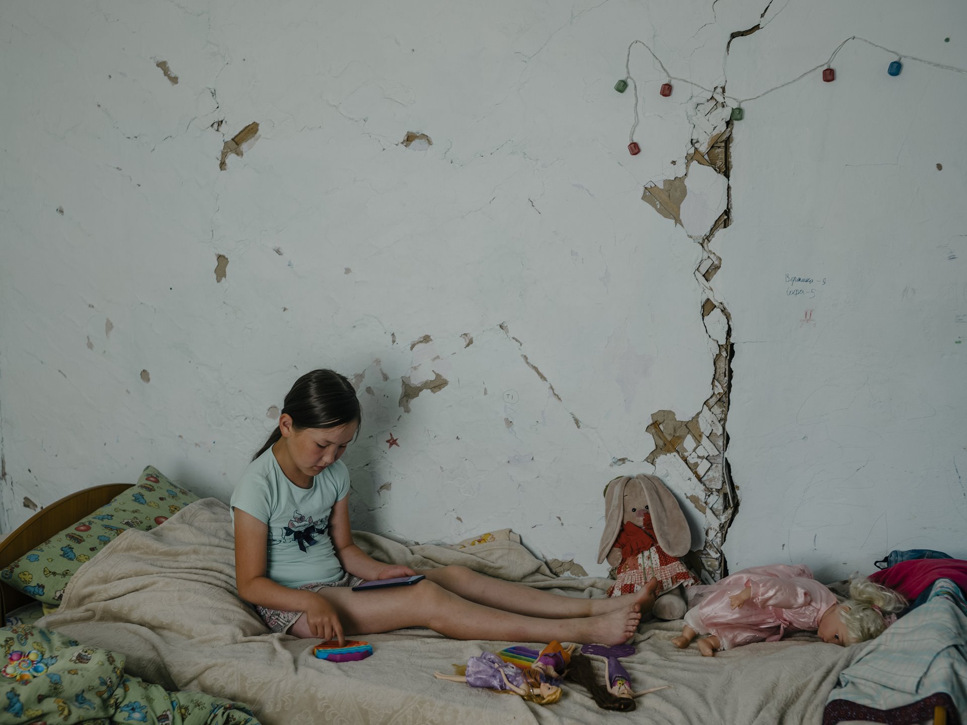 Veronika in her room in Yunkyur, in southern Sakha, Siberia, Russia. As with other village houses, the foundations of her family&rsquo;s home are being undermined by thawing permafrost. The floor is sinking, cracks run through the walls, and the basement where the family stored potatoes has collapsed.