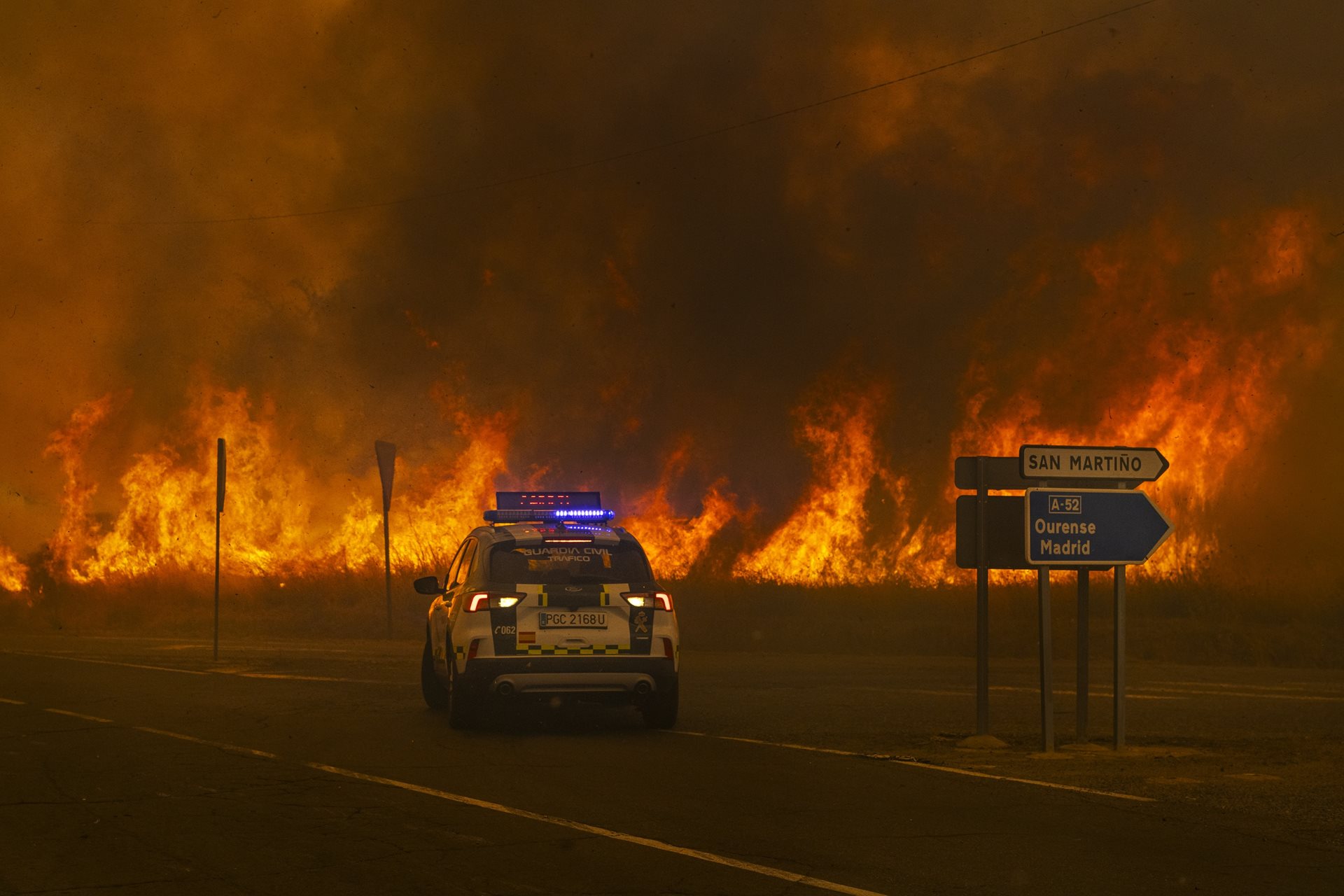 A Spanish Civil Guard vehicle reverses away from advancing flames at the access road to the Ourense&ndash;Madrid Highway in Cualedro, as wildfires cut off roads across the region. Ourense, Galicia, Spain