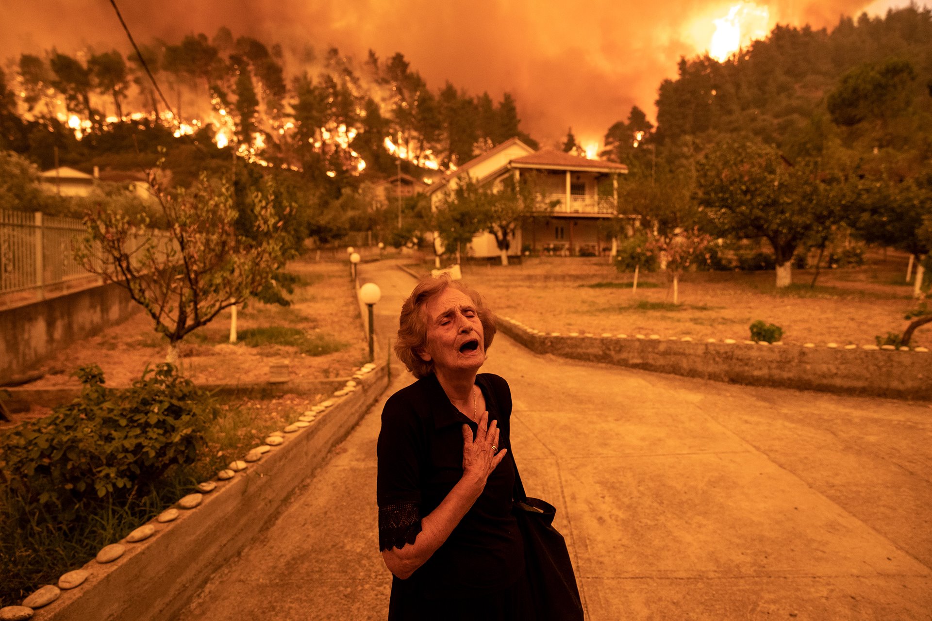 Panayiota Kritsiopi cries out as a wildfire approaches her house in the village of Gouves, on the island of Evia, Greece.