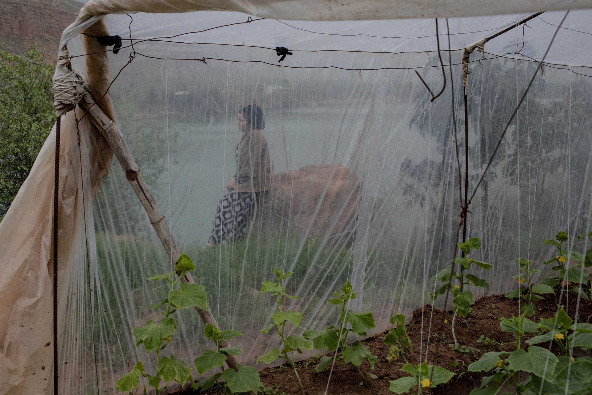 An inhabitant of the village Istiqlol, Tajikistan, rests beside her greenhouse on the River Vakhsh, a tributary of the Amu Darya. She uses river water to irrigate her cucumbers.
