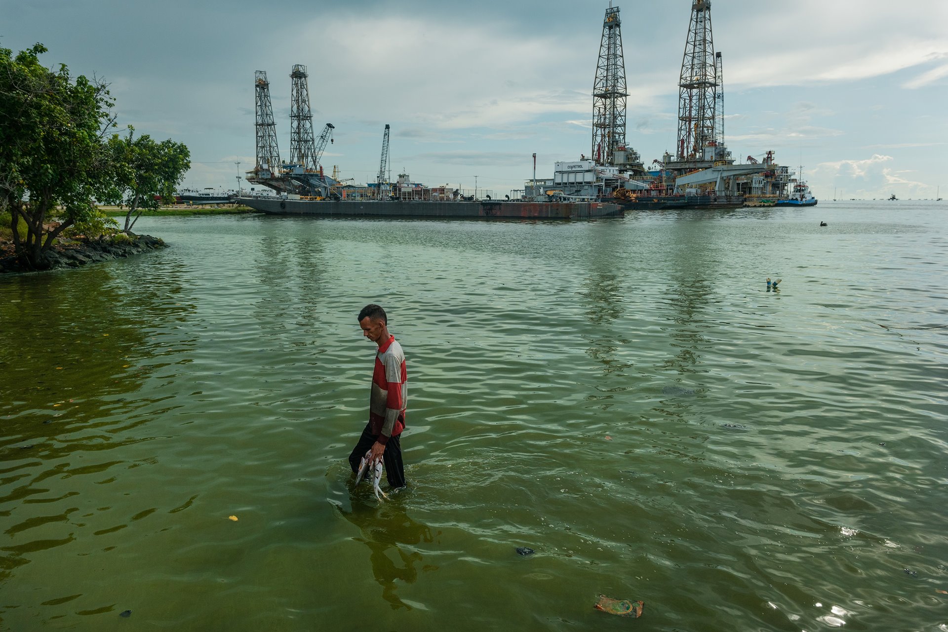 Wilmer Parra (32), with a handful of fish he caught in Lake Maracaibo, Cabimas, Venezuela, walks from his boat to shore through waters covered in algae. The nation&#39;s largest oil fields are located around and beneath Lake Maracaibo. Along with oil slicks, the lake has become covered with algae caused by discharged fertilizers, sewage, and other chemicals.&nbsp;