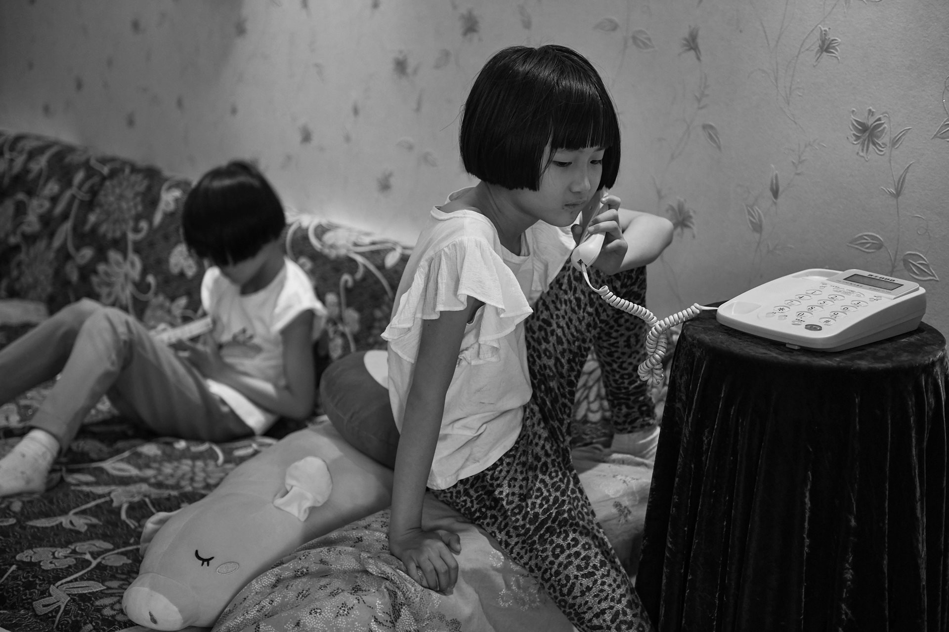 Huihui (8) calls her mother, asking when she will be home from her business trip. Although many of her peers had retired, Sheng Hailin continued to work to support her daughters. Hefei, Anhui Province, China.&nbsp;