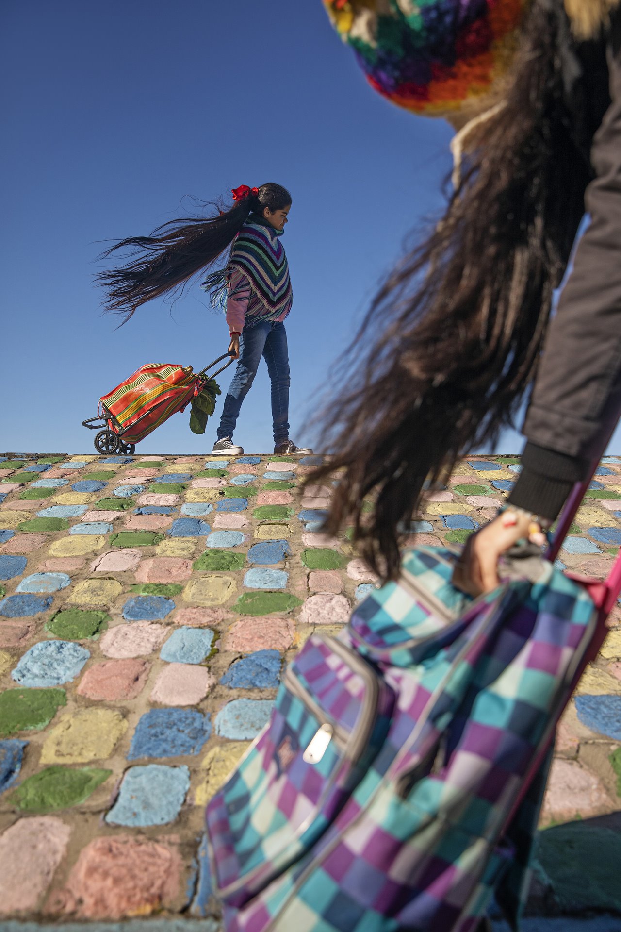 Antonella (in the background) shops for groceries in La Boca neighborhood, on the outskirts of Buenos Aires, Argentina, at a time when her school had still not resumed in-person lessons, but others had. In the foreground, students attending in-person school pass by. At the time, the City of Buenos Aires contested a federal government lock-down ruling for schools, but Antonella lived 500 meters beyond city jurisdiction.