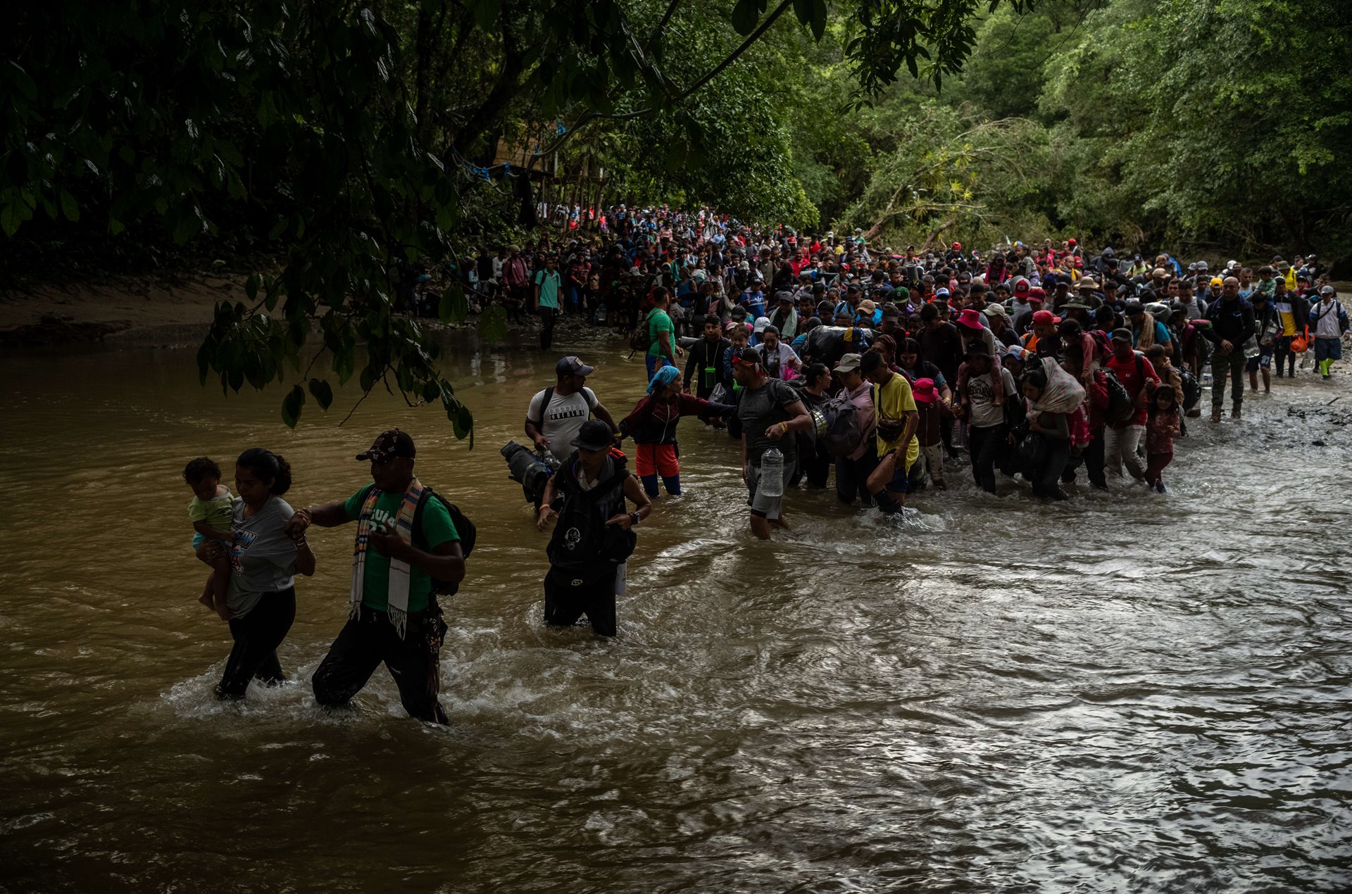 Thousands of migrants wade into the Rio Muerto (&ldquo;Death River&rdquo;) at the Darién Gap, where several have drowned in its treacherous waters. They assist one another to prevent drowning in the swift currents. Rio Muerto, Colombia.