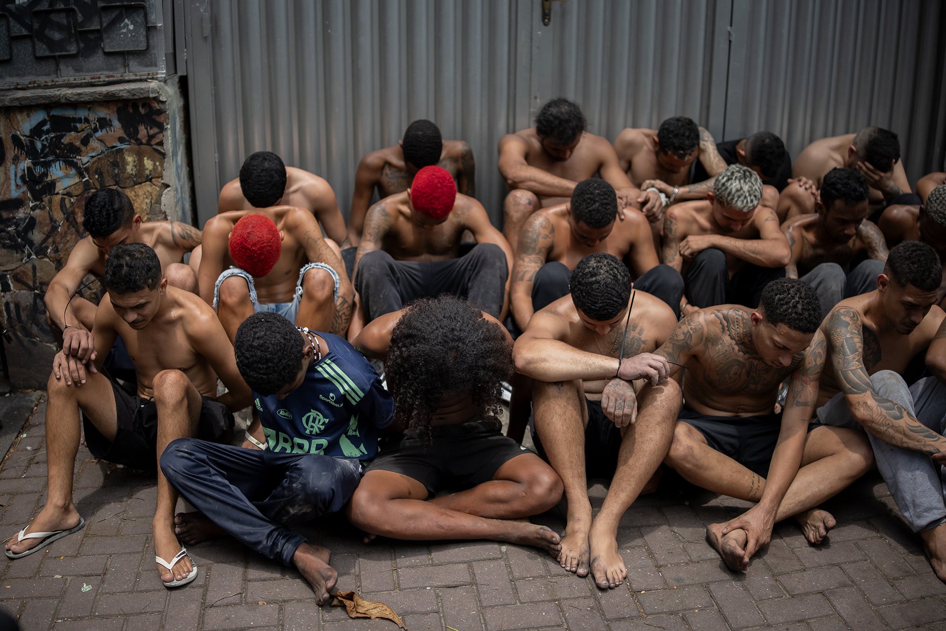 Detained suspects wait with bowed heads to protect their identities and prevent communication. Of the 100 arrest warrants that precipitated the raid, only a few were successfully executed. Rio de Janeiro, Brazil.