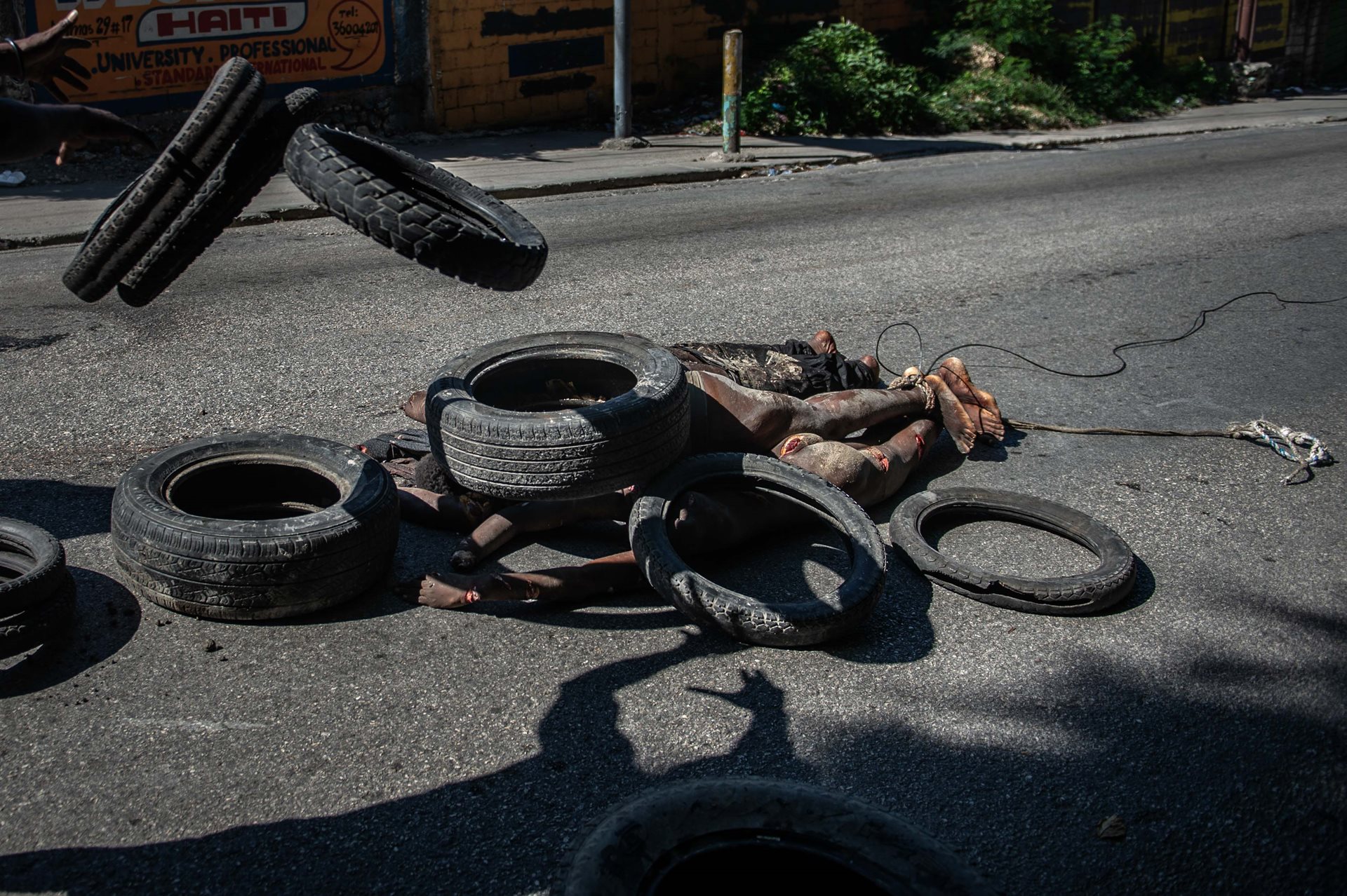 A local resident throws tires on the bodies of suspected gang members killed by police, in Pétion-Ville, Port-au-Prince, Haiti.