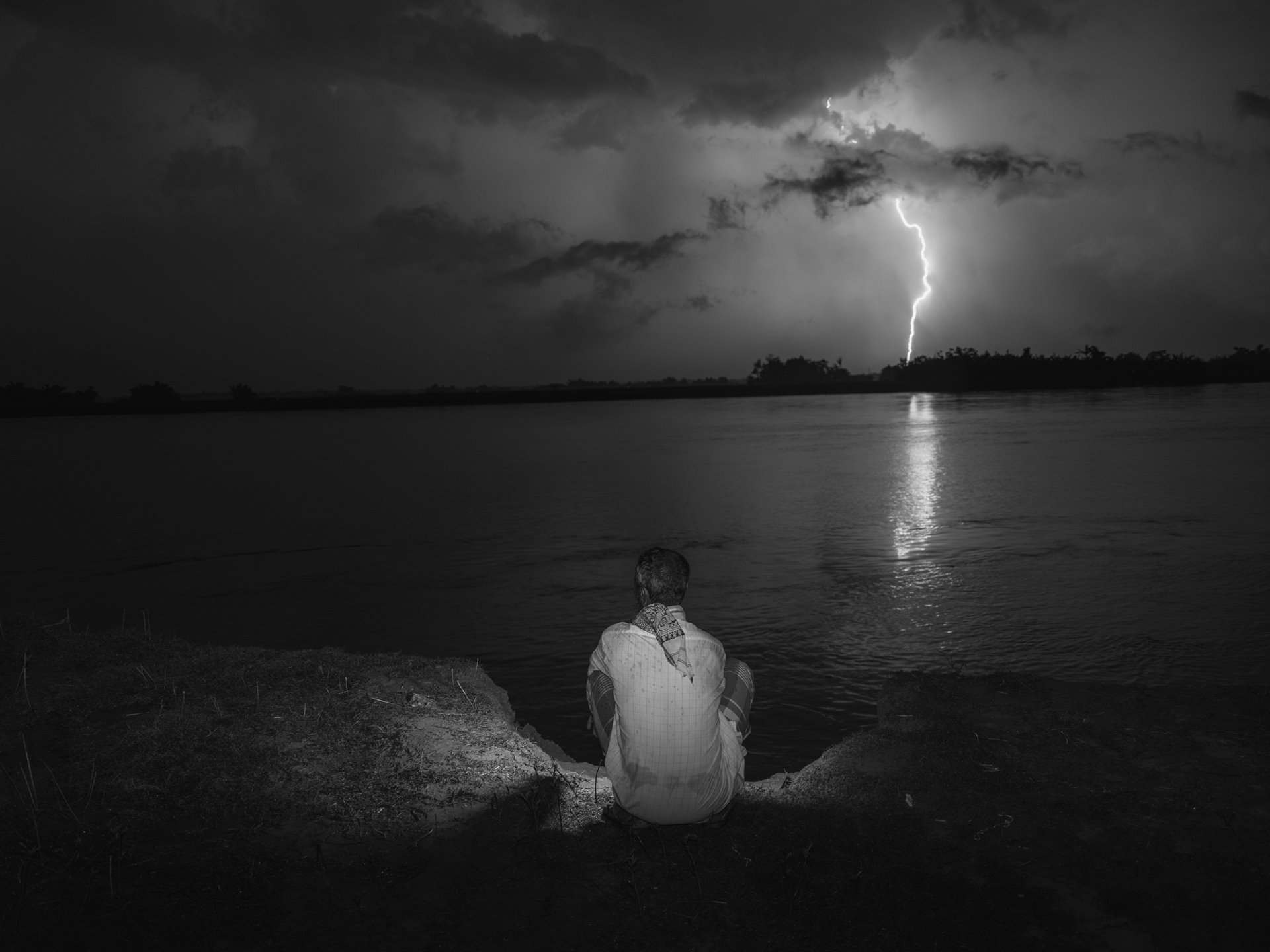 Kabod Ali, a Bengali Muslim from Kharbali village, often ventures to the Beki riverbank for mobile network access. The Beki, a Brahmaputra tributary, threatens flash fooding during the monsoon season. According to Ali, his mother narrowly survived an incident where she was mistaken for an immigrant and thrown into the river by border police. Devastating floods exacerbate the plight of Assam&#39;s Bengali Muslim community, who face environmental devastation as well as a struggle for citizenship and recognition by the state. Kharbali West, Barpeta, Lower Assam, India.