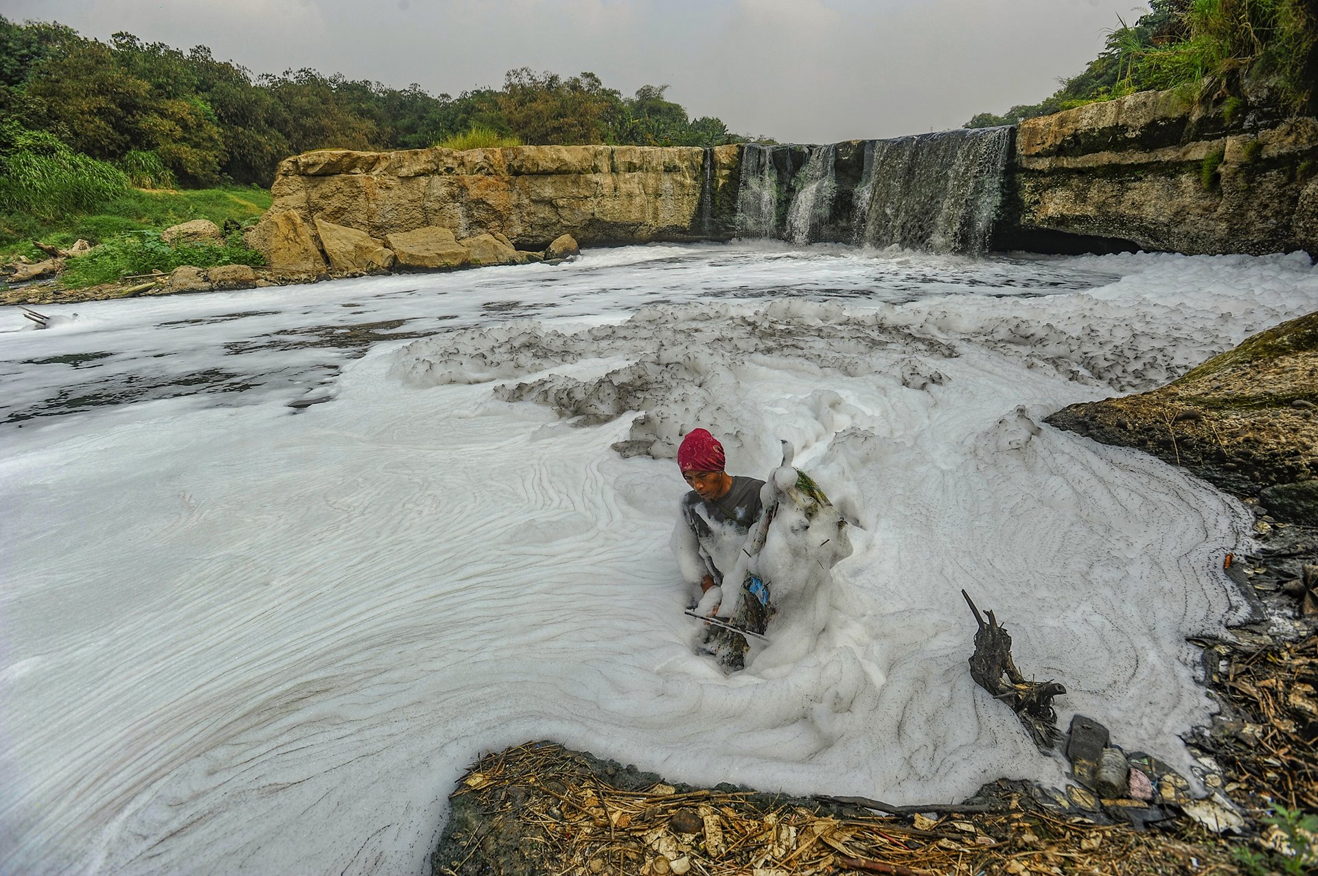 A resident catches fish at a once-scenic waterfall on the Cileungsi River. The thick foam on the water is largely a product of waste runoff from nearby industries. Curug Parigi, Indonesia.