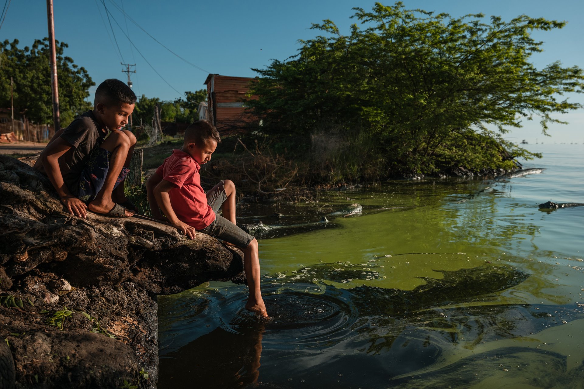 Luis Javier (9) and Luis David (8) play on the shores of Lake Maracaibo, Cabimas, Venezuela, which is stained with algae and crude oil. The nation&#39;s largest oil fields are located around and beneath Lake Maracaibo. Along with oil slicks, the lake has become covered with algae caused by discharged fertilizers, sewage, and other chemicals.&nbsp;