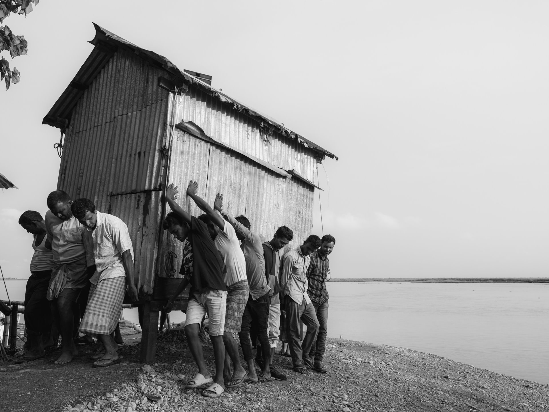 Bengali-speaking Hindus and Muslims help each other shift shops from the edge of the Brahmaputra river at the Tarabari ferry point. The shifting is done in anticipation of the erosion of land that occurs with each monsoon season, which is often devastating for residents as they are forced to constantly adapt to a changing landmass each year. Tarabari, Bahari constituency, Barpeta district, Lower Assam, India.