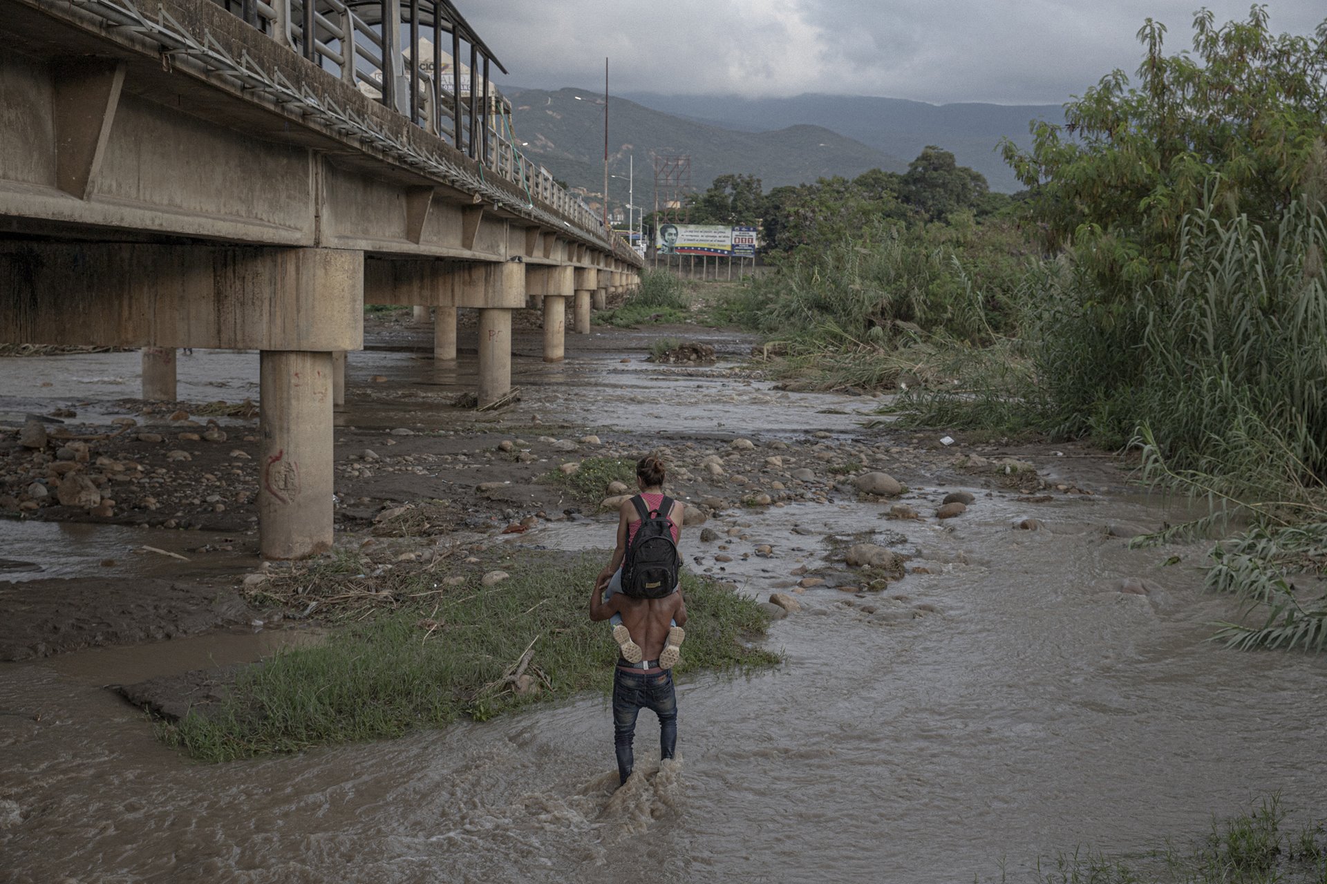 <p>A man carries a woman across the Táchira River, which forms the Venezuela-Colombia border. Bridges were closed due the COVID-19 pandemic. UNHCR reported that Colombia hosted some 1.8 million Venezuelan refugees and migrants by May 2022, the largest portion of the diaspora.&nbsp;</p>
