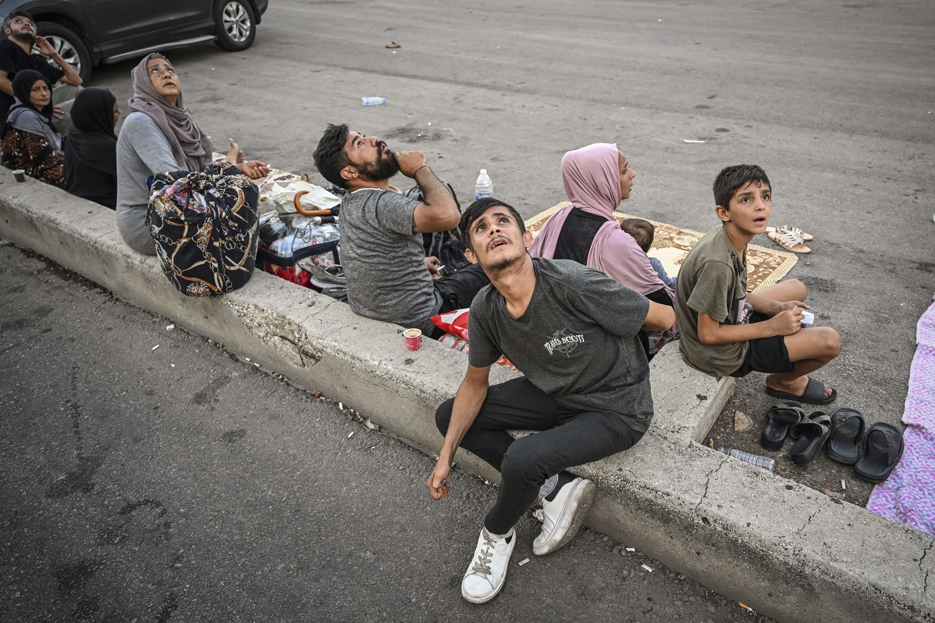 People glance anxiously upwards during an Israeli drone strike, as they take refuge away from buildings in Beirut&#39;s Dahiyeh neighborhood, Lebanon. Jets and drones often fly at low altitudes, causing fear and distress.<br />
&nbsp;