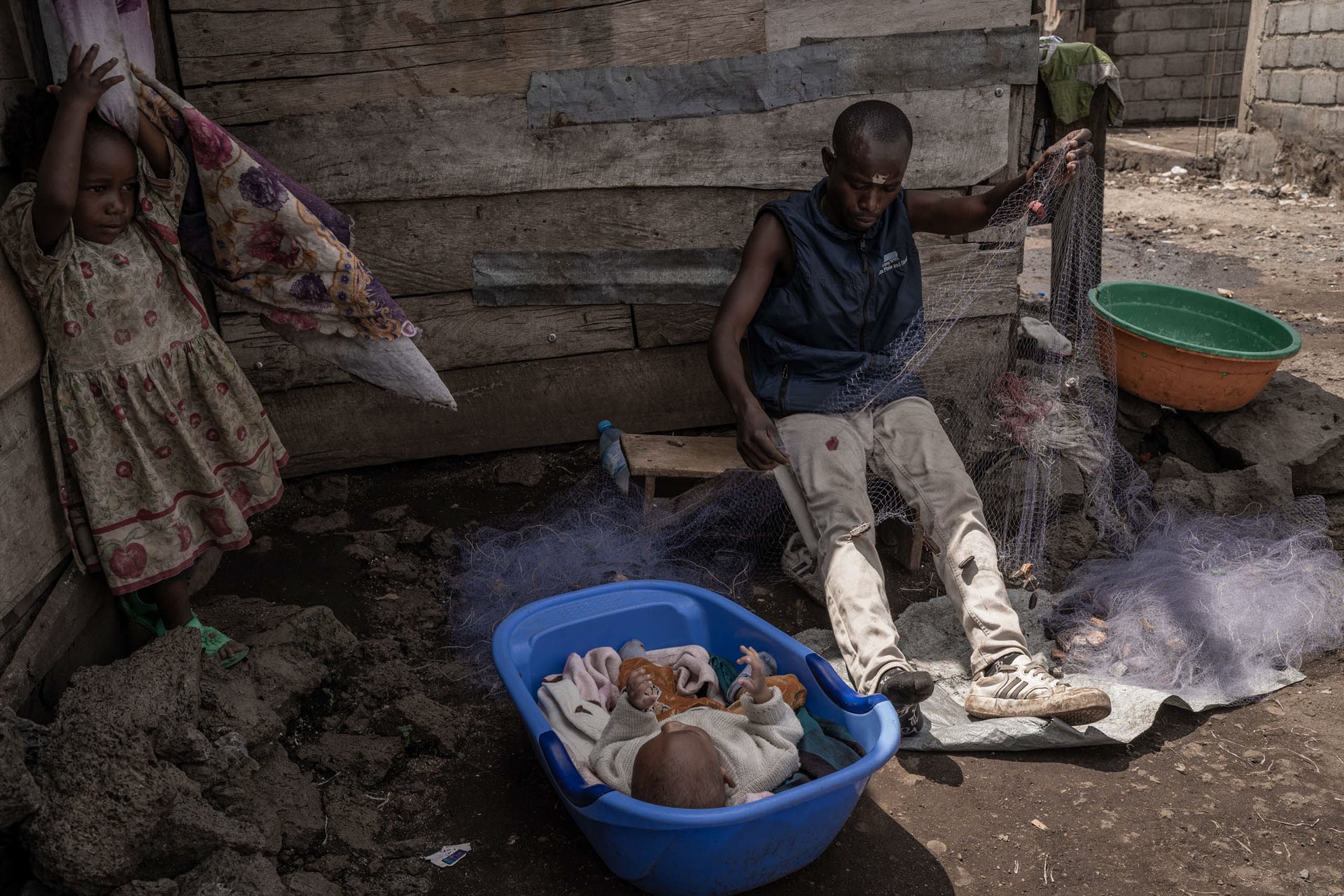 Emanuel Chabala (33) watches over two of his five children while arranging his nets in front of his home, in Goma, DRC.