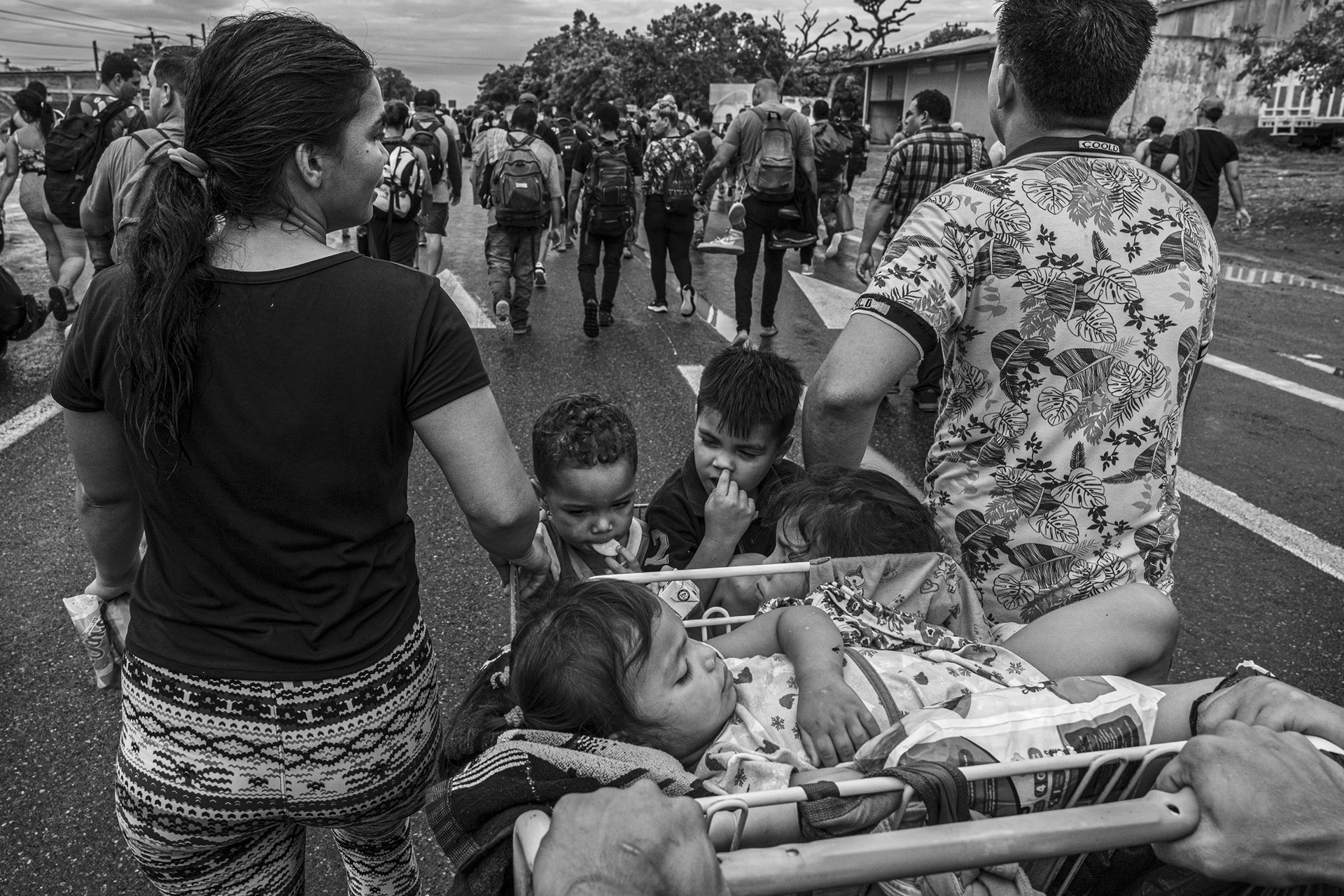 Martinez&#39;s family pushes a supermarket cart with children aboard as they depart from Tapachula, Mexico, alongside a migrant caravan primarily composed of Venezuelans. Tapachula, near the border with Guatemala, serves as a compulsory stop for migrants and asylum seekers because one of the offices of the Mexican Commission for Aid to Refugees (COMAR) is located in the city. Local NGOs accuse COMAR of corruption: selling humanitarian visas to those who can afford them and deliberately delaying visas to others to curb the influx of migrants toward the US-Mexico border.