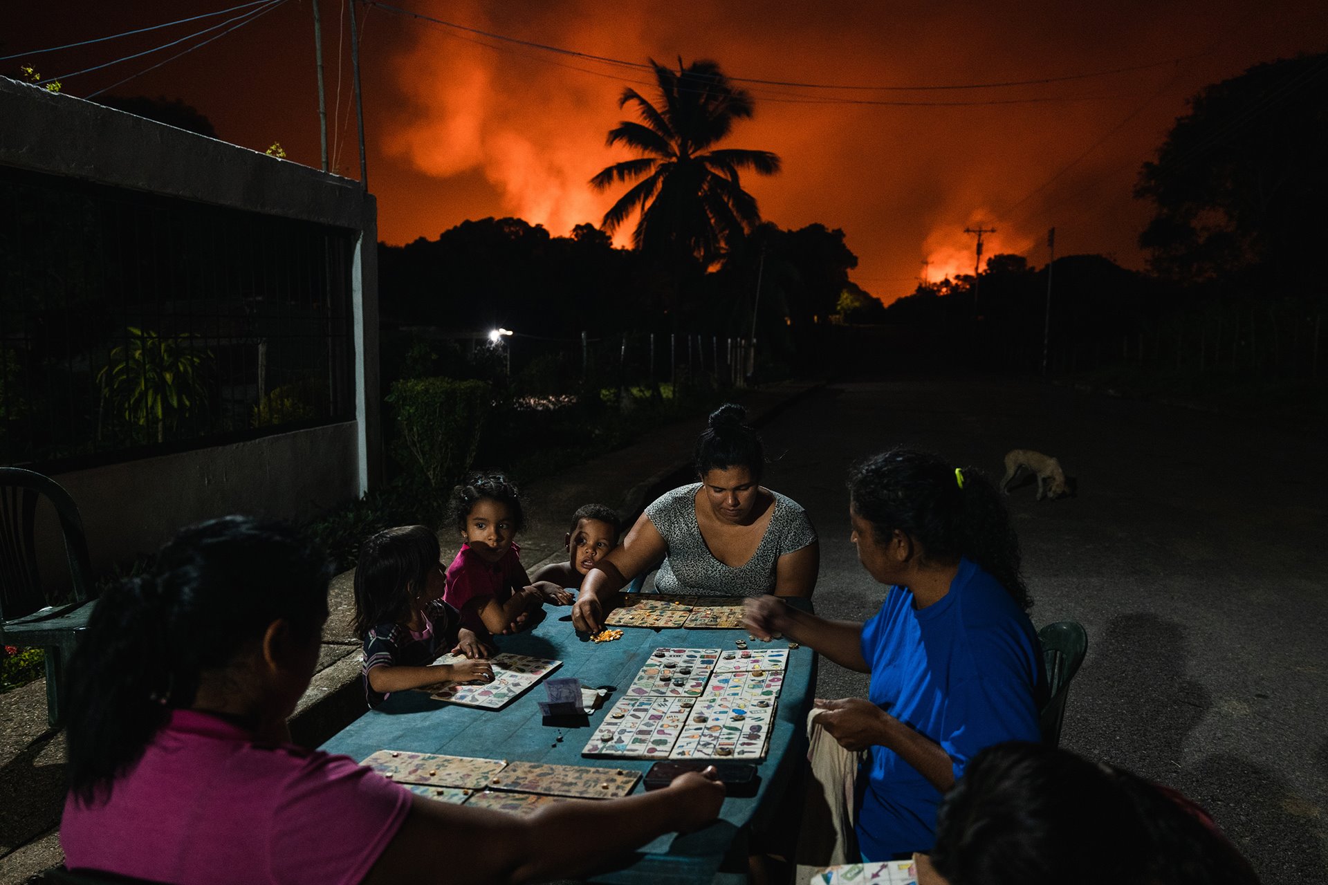 Neighbors play Animal Lotto under a sky lit by one of the world&rsquo;s largest gas flares (the flaming chimneys used to burn off excess natural gas at oil wells), in Punta de Mata, Venezuela.&nbsp;