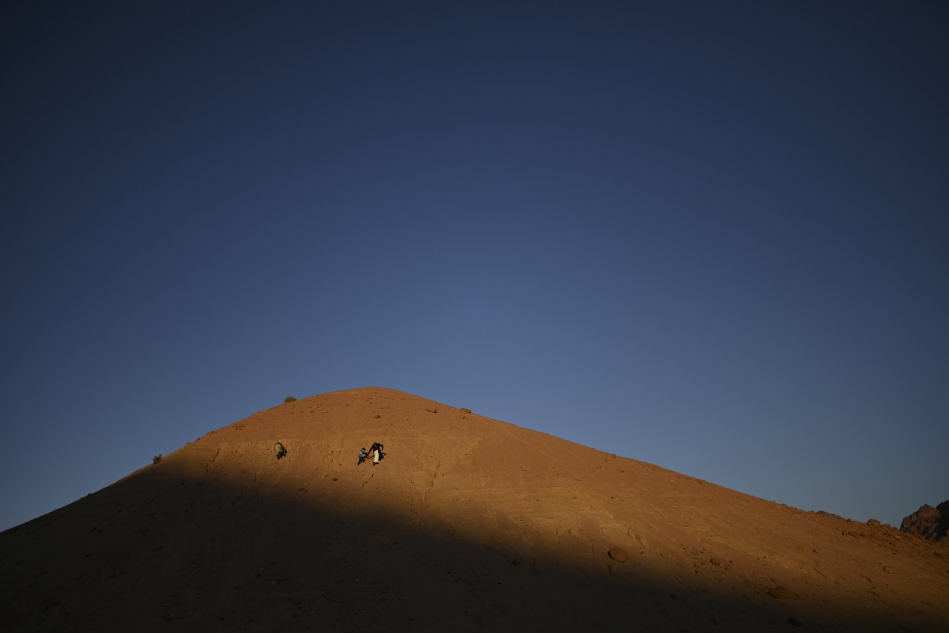 A father and son walk over a hill in the Gharba Valley to watch the lost moments of sunset in St. Catherine, South Sinai, Egypt. The role of the father in Bedouin family dynamics extends beyond providing food for the family. Fathers also stay at home while the mothers are away walking the village herd.
