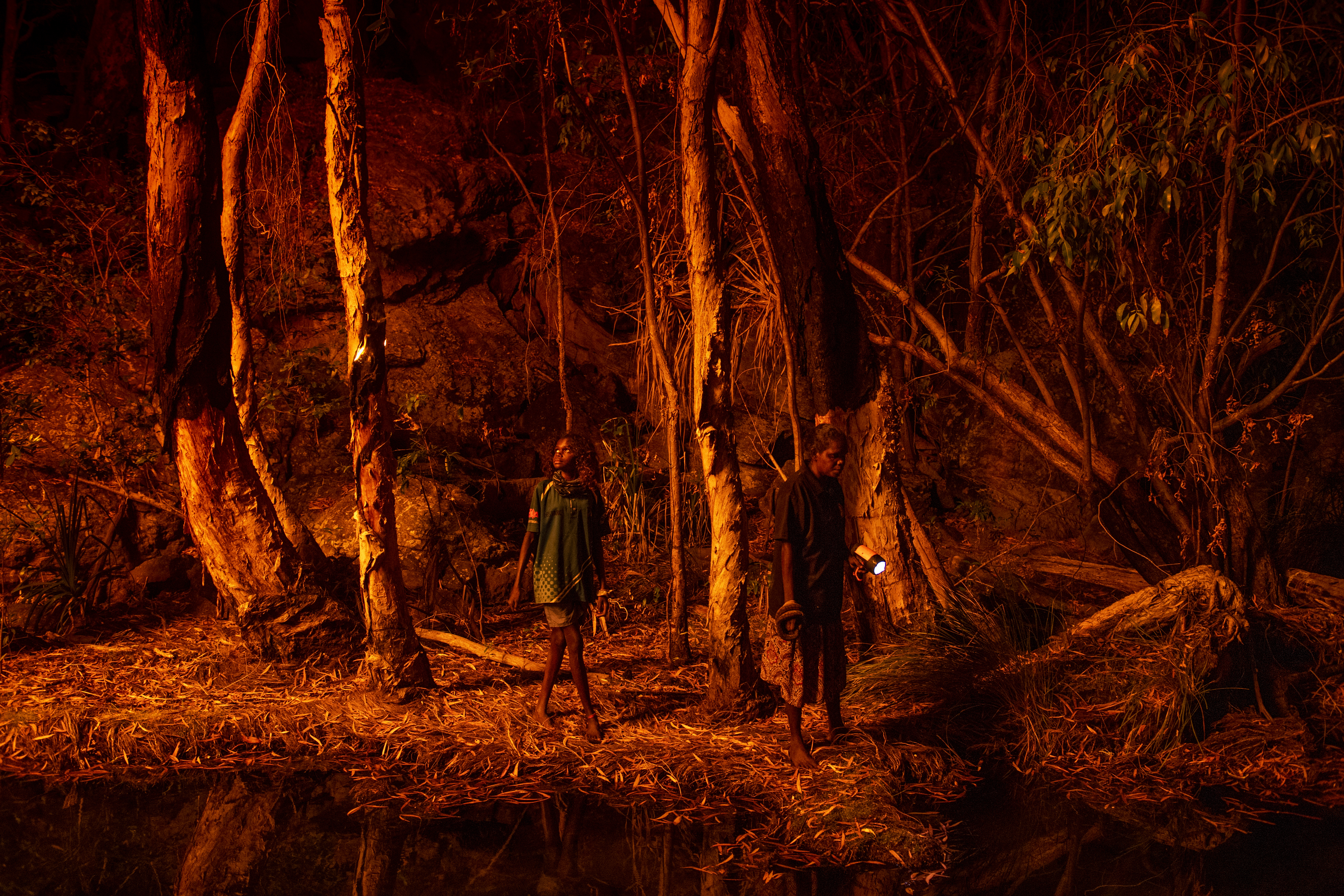 Stacey Lee (11, left) sets the bark of trees alight to produce a natural light source to help hunt for file snakes <i>(Acrochordus arafurae)</i>, in Djulkar, Arnhem Land, Australia.