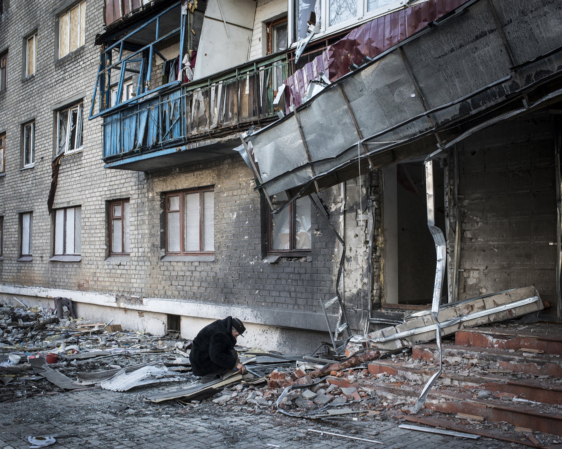 Alexi Stipanovich crouches outside the building where he lives, which was hit by shells in fighting between Ukrainian and pro-Russian forces, in Debaltseve, Donbas, Ukraine.