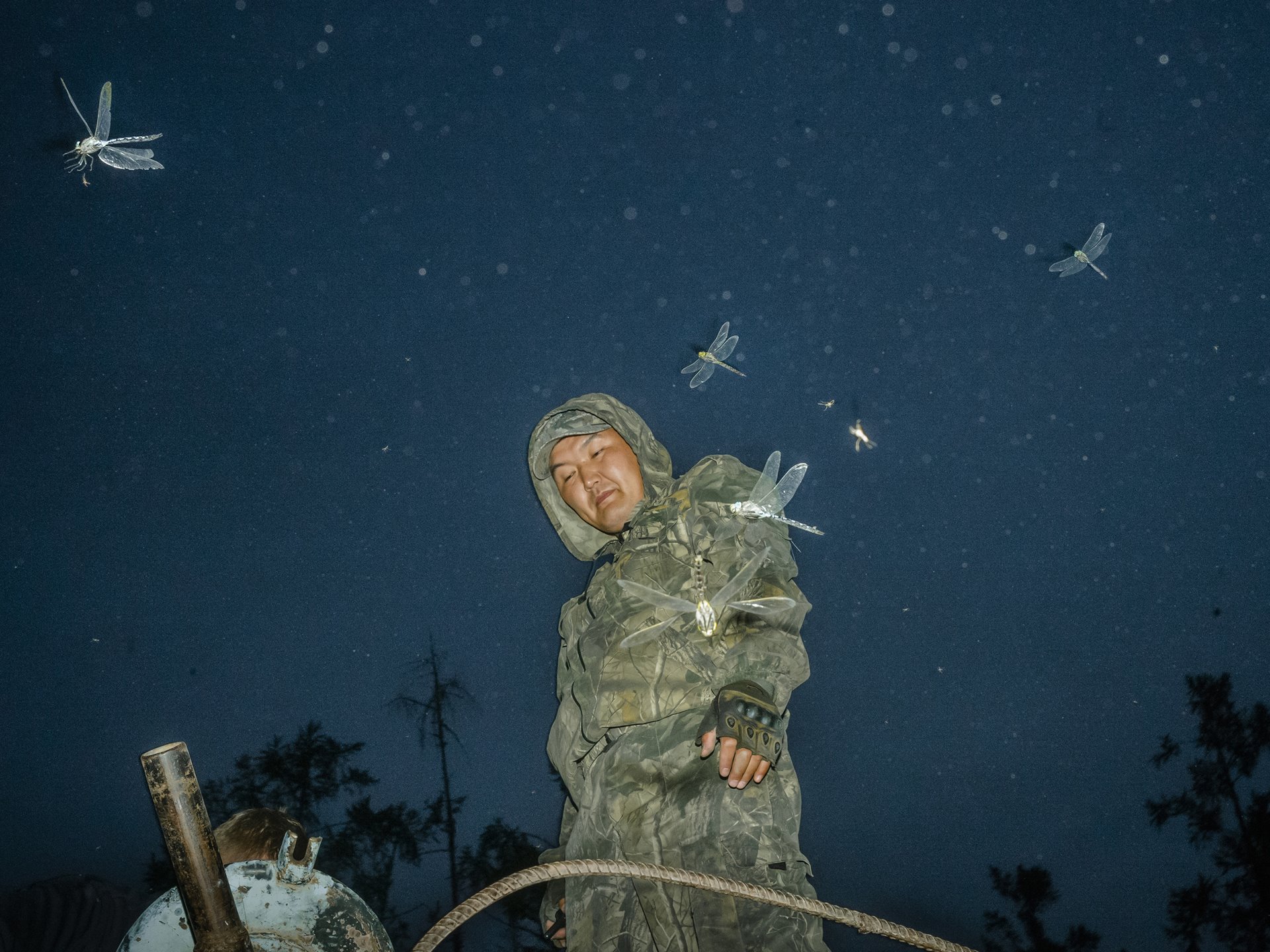 Dragonflies catch mosquitoes, while a local volunteer firefighter pumps water from a lake into a water truck before driving to a forest fire near Bulgunnyakhtakh, Sakha, Siberia, Russia.