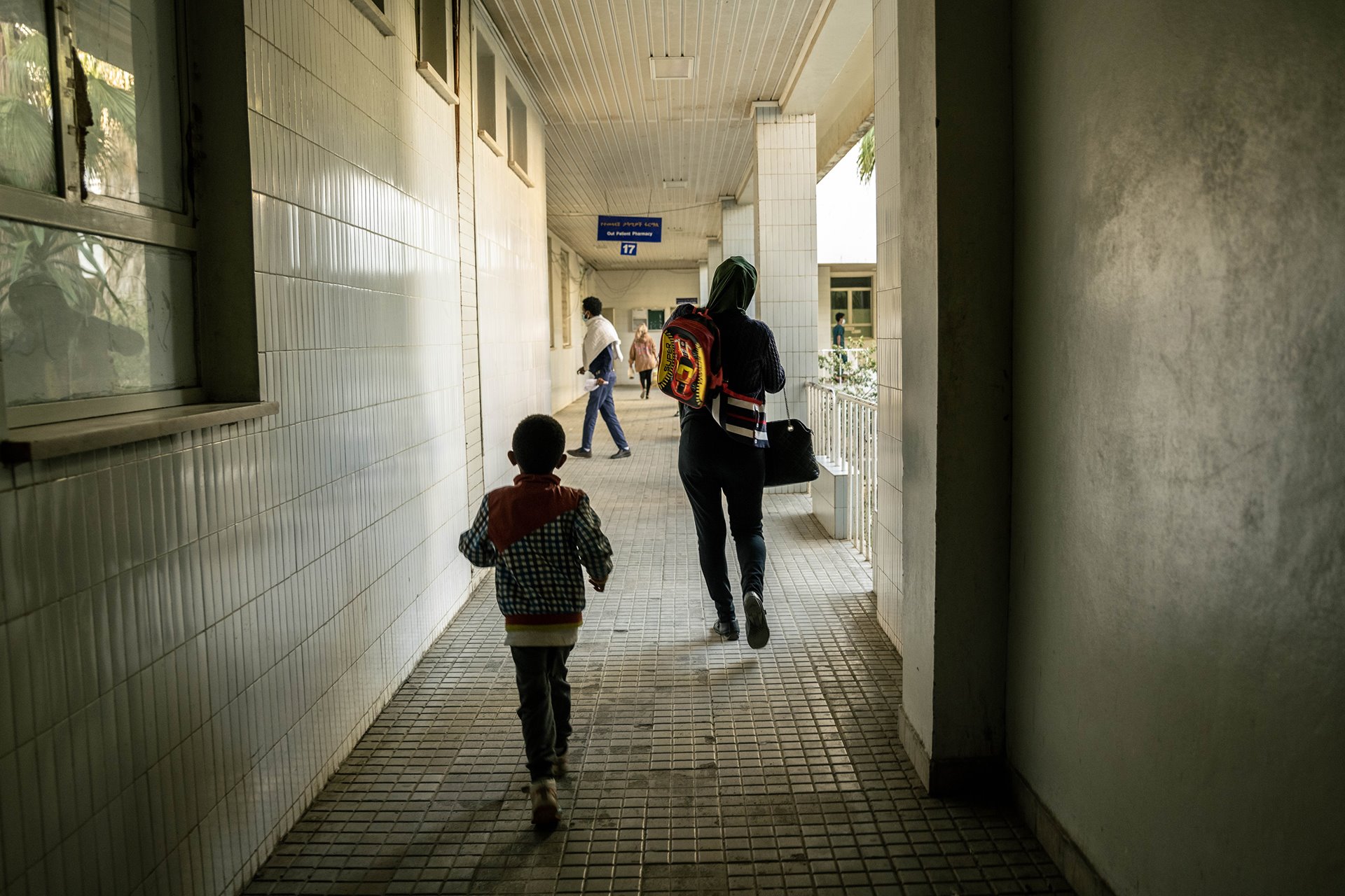 Shila (32) and her son walk down a corridor of Ayder Hospital for a medical appointment in Mekele, Ethiopia. Ayder Hospital is the largest hospital in Tigray. During the war it was cut off from supplies and struggled to serve a massive influx of trauma patients.