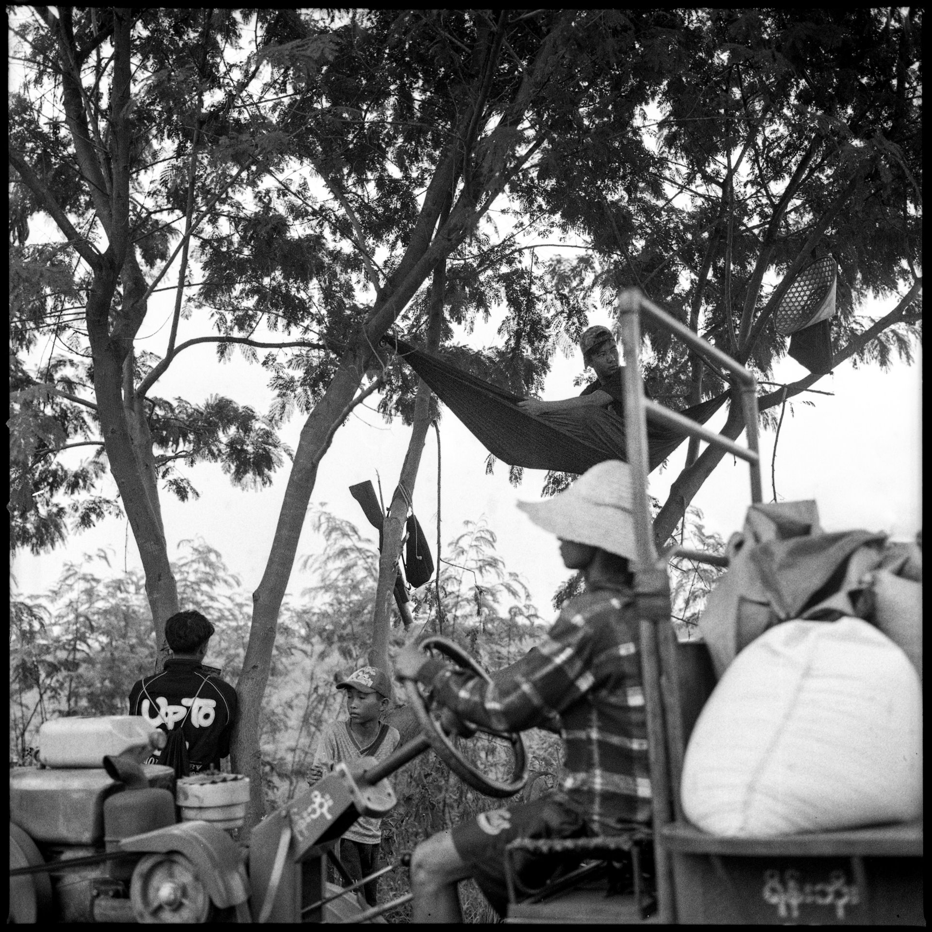 A resident of the strategically important and highly contested town of Moe Bye, in Shan State, Myanmar, drives by on his tractor, while fighters from resistance forces secure the area. Villagers had decided to resume farming to protect their livelihoods, despite the risk of artillery shelling and landmines from the Myanmar military.