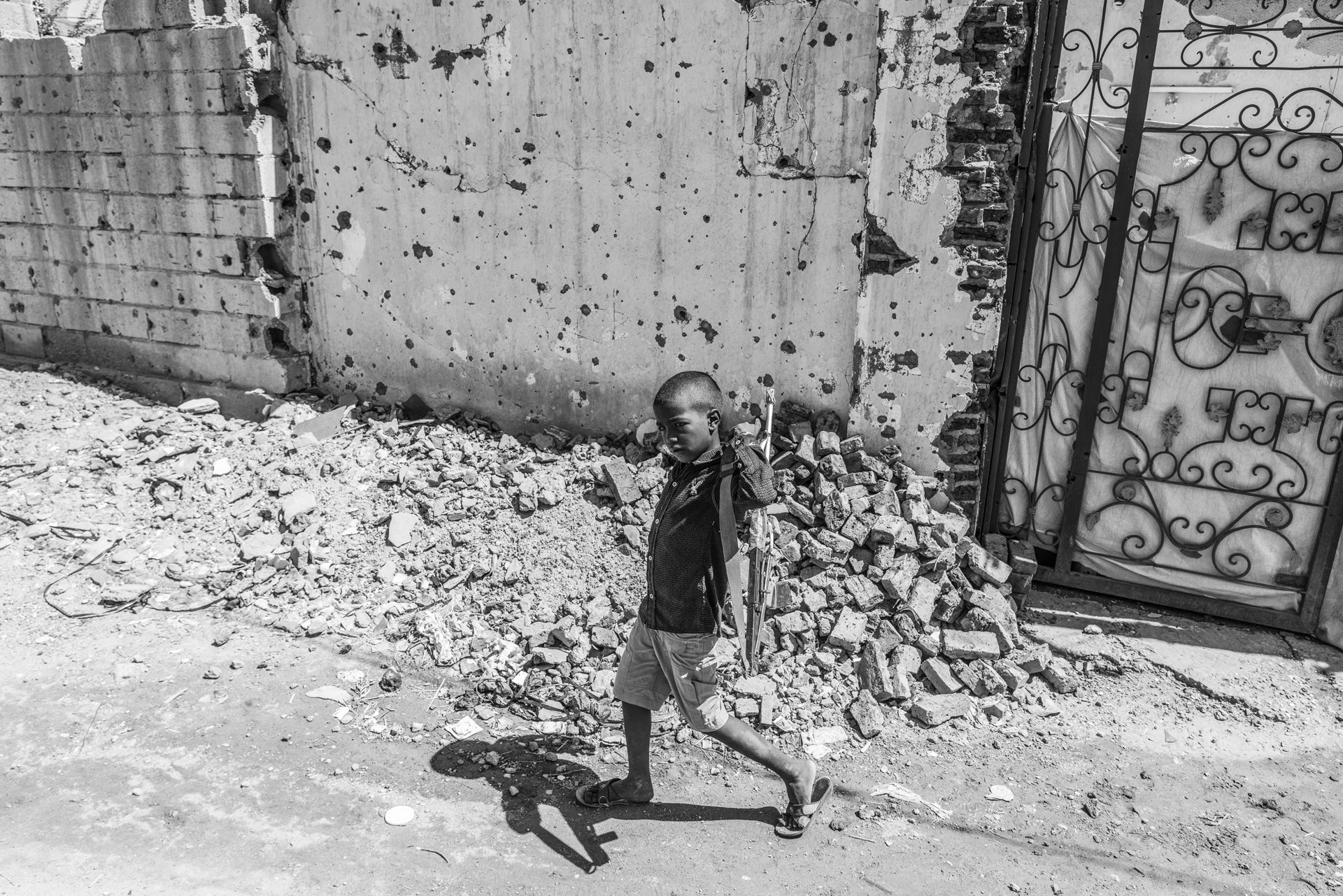 Omar holds a toy Kalashnikov as he leaves his damaged home in the Wad Nubawi neighborhood of Omdurman in Sudan.<br />
&nbsp;