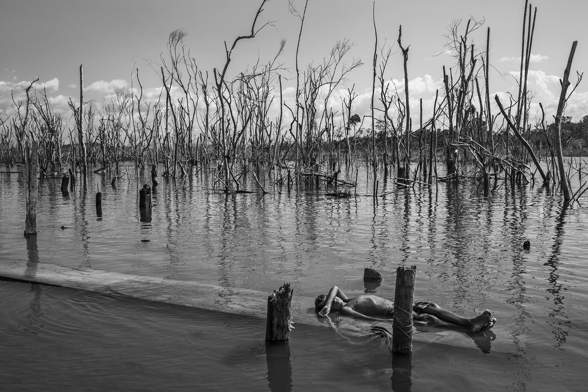<p>A boy rests on a dead tree trunk in the Xingu River in Paratizão, a community located near the Belo Monte hydroelectric dam, Pará, Brazil. He is surrounded by patches of dead trees, formed after the flooding of the reservoir.</p>
