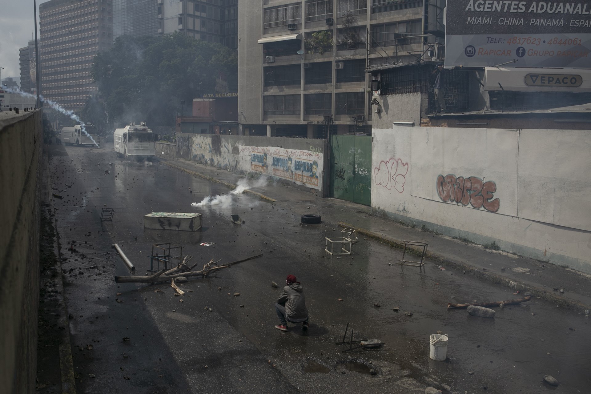 A man squats in the street following clashes between anti-government protesters and security forces using water cannons, in Caracas, Venezuela.