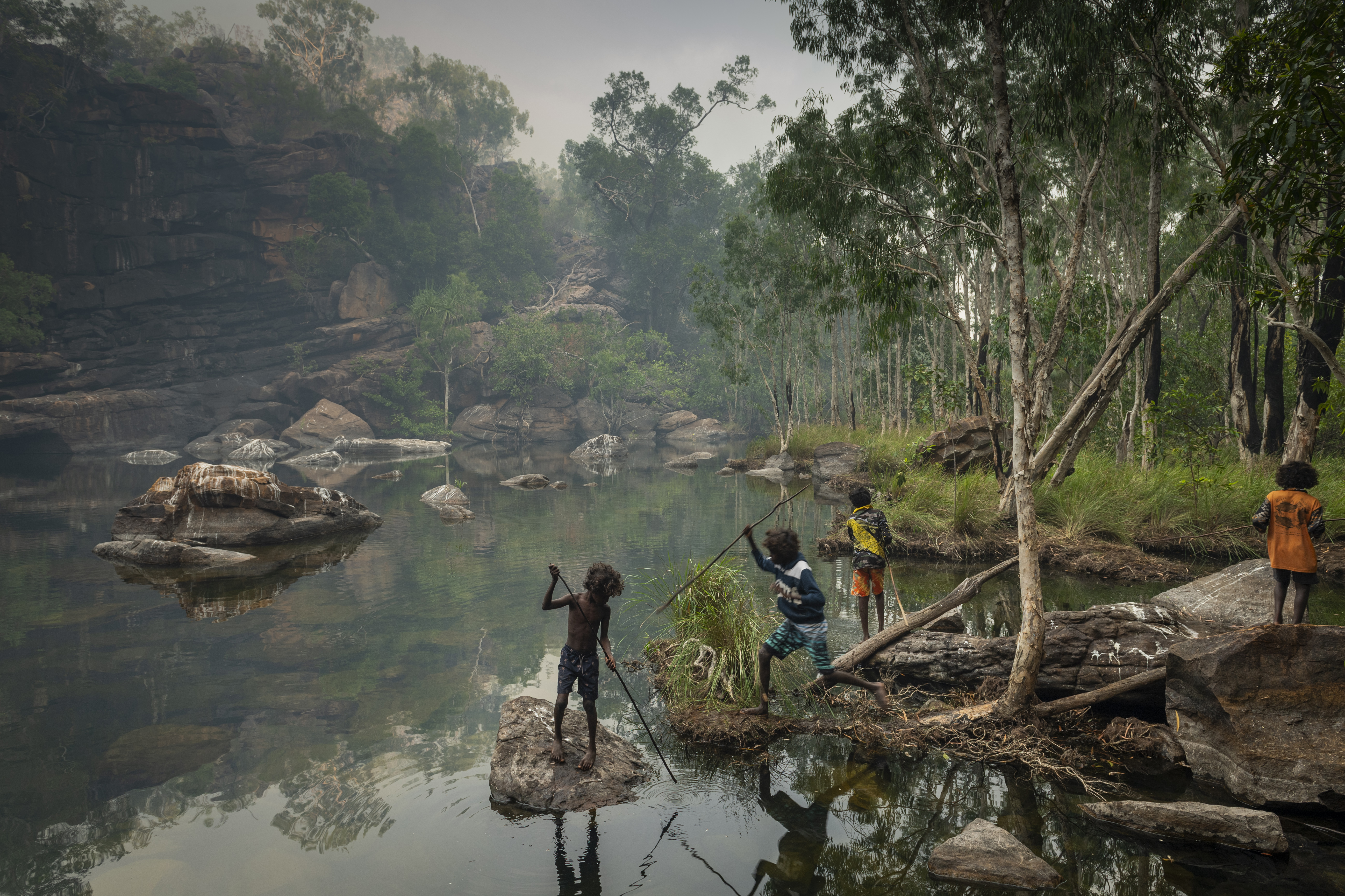 A group of children spear fish early one morning near Djulkar Waterfall, Arnhem Land, Australia, on 23 July 2021. Smoke from a fire that was lit the previous day still hangs in the air.