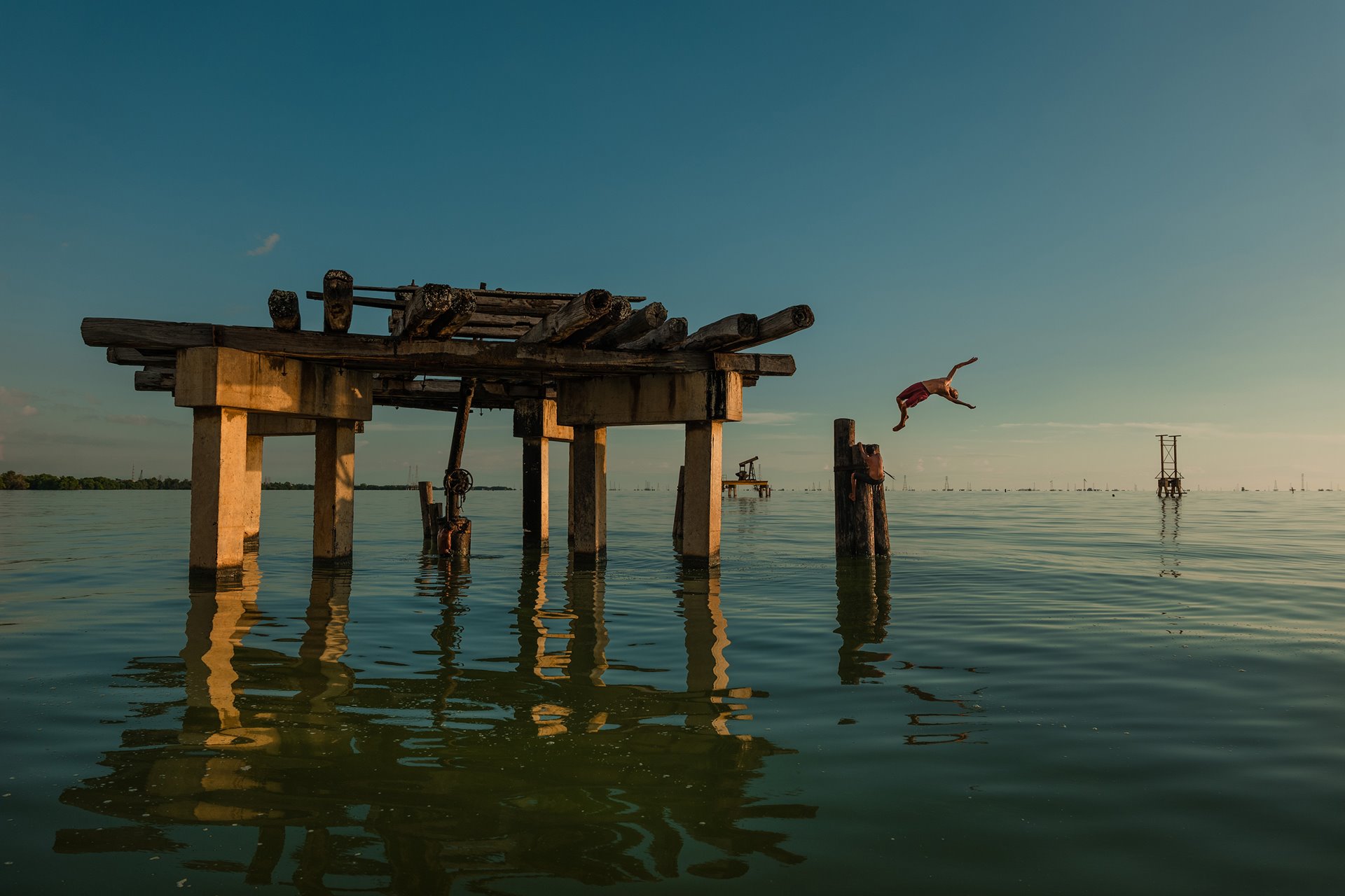 Yon Medina dives from an abandoned oil rig into Lake Maracaibo, Cabimas, Venezuela. The nation&rsquo;s largest oil fields are located around and beneath the lake, which is covered with algae caused by discharged fertilizers, sewage, and other chemicals.&nbsp;