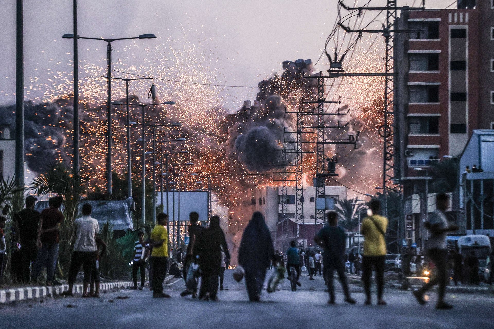 People watch as smoke and flames rise over a building, following Israeli attacks on Deir al-Balah, Gaza. Israel bombarded the central Gazan city multiple times through the year.&nbsp;
