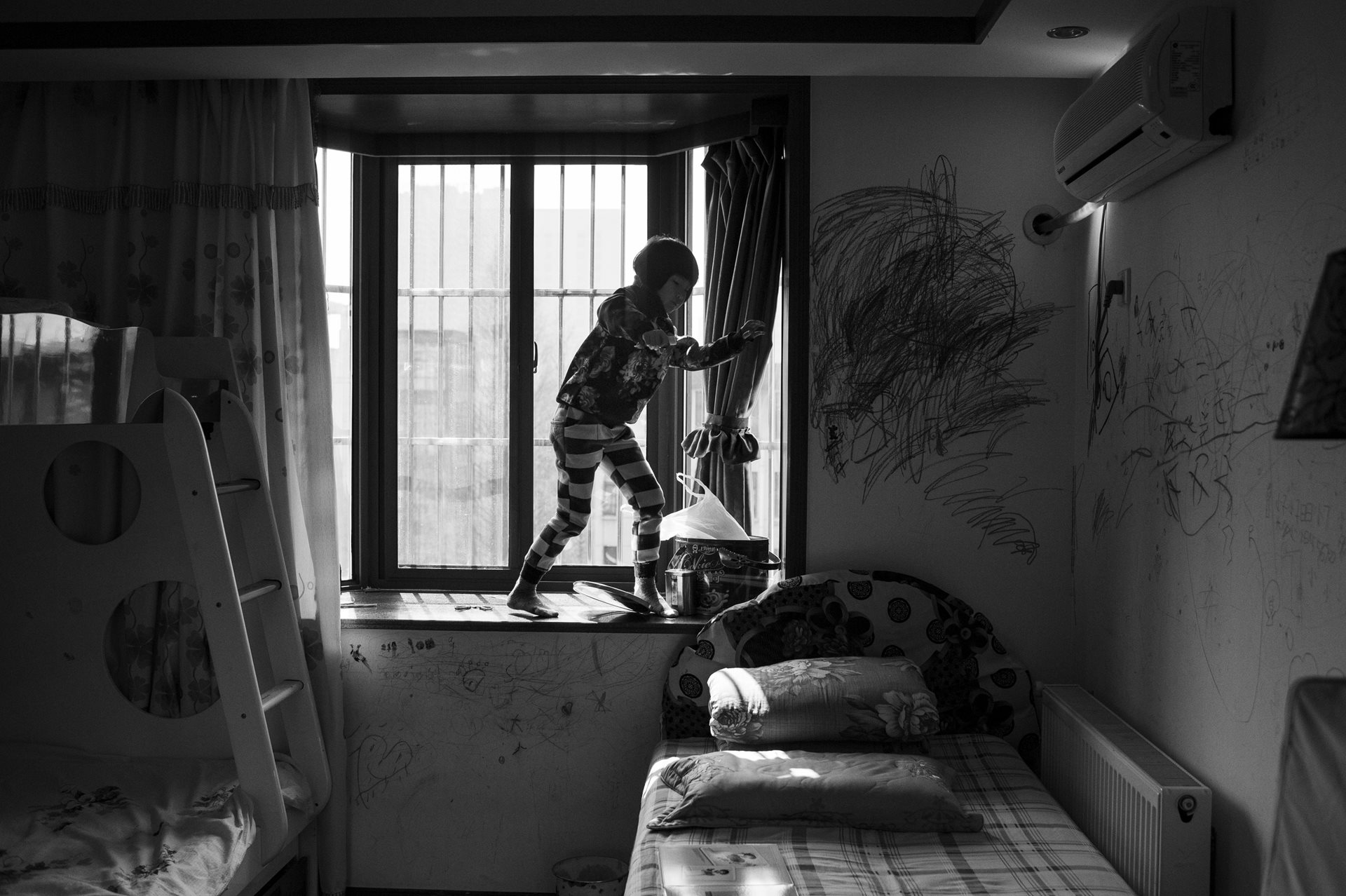 Huihui plays on a windowsill decorated with drawings by the sisters. Hefei, Anhui Province, China.