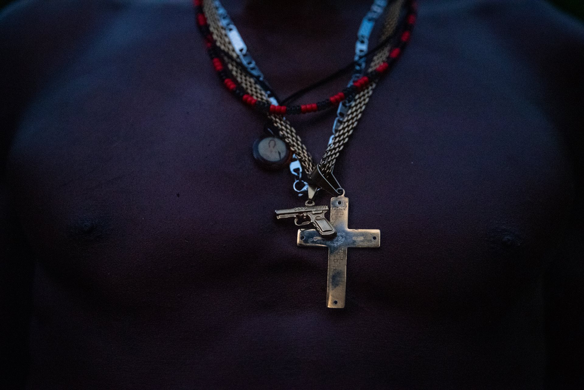 A man displays chains featuring a gold weapon and a cross in Juntas, Buenaventura, Colombia. Guerilla, paramilitary, and drug cartel groups contest this region of the Yurumanguí River for control of illicit activities like coca cultivation and mining. Their clashes lead to the displacement of hundreds from the area.