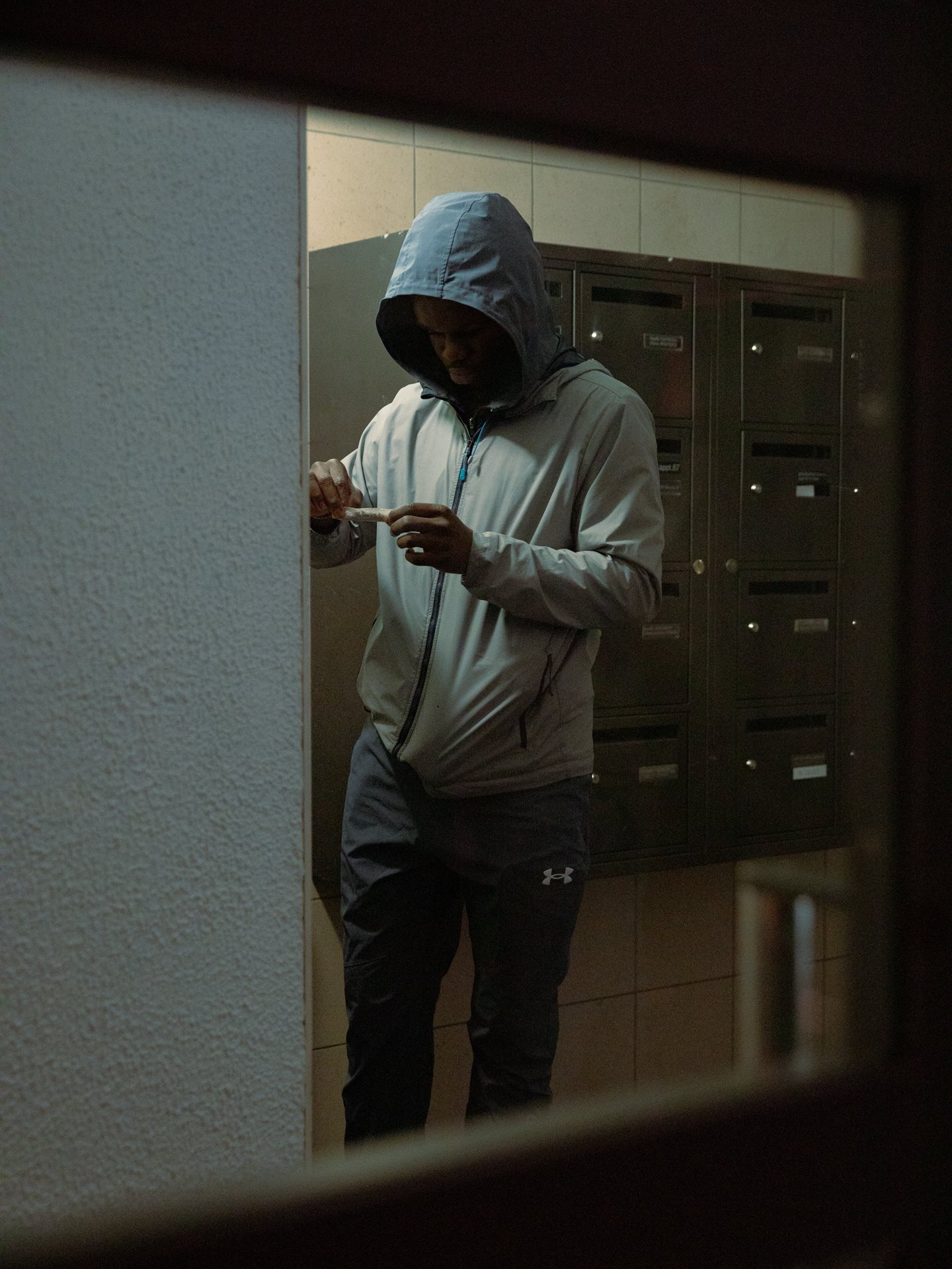 A young man, part of a drug dealing operation, rolls cannabis resin in the hallway of a building in a housing project in Seine-Saint-Denis, France, where mailboxes are sometimes used to hide merchandise.