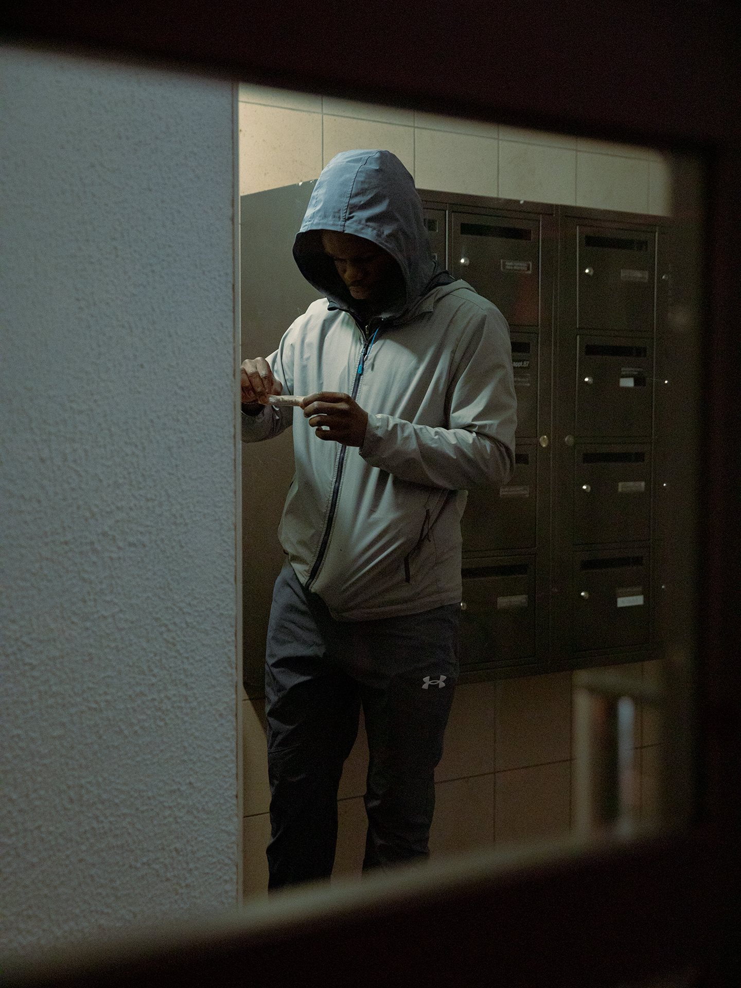 A young man, part of a drug dealing operation, rolls cannabis resin in the hallway of a building in a housing project in Seine-Saint-Denis, France, where mailboxes are sometimes used to hide merchandise.