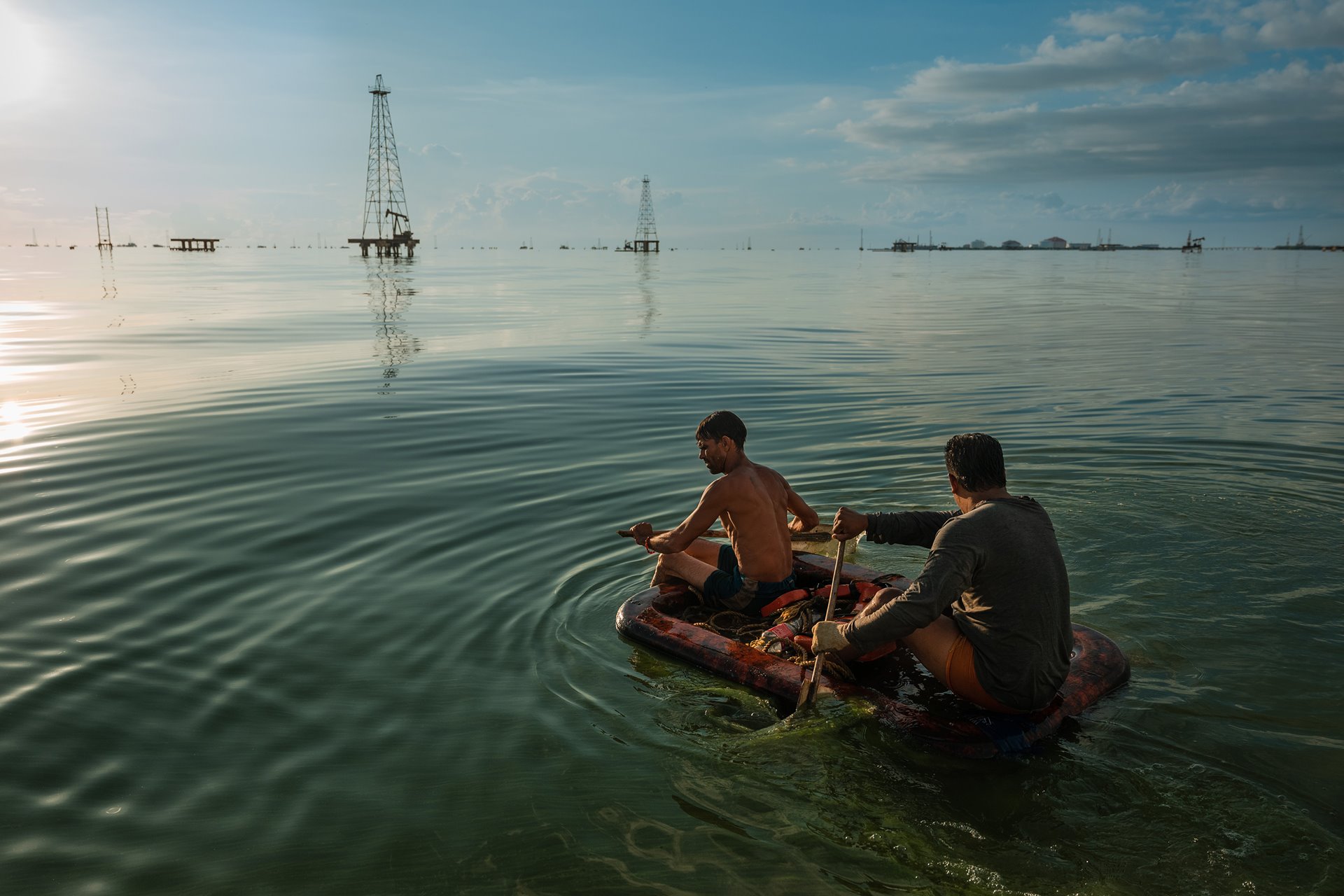 Two fishermen paddle through the green waters of Lake Maracaibo, Cabimas, Venezuela, which along with oil, has become covered with algae caused by discharged fertilizers, sewage, and other chemicals. The fish they catch are sometimes stained with crude oil, and fishermen are forced to clean it with gasoil before eating it.