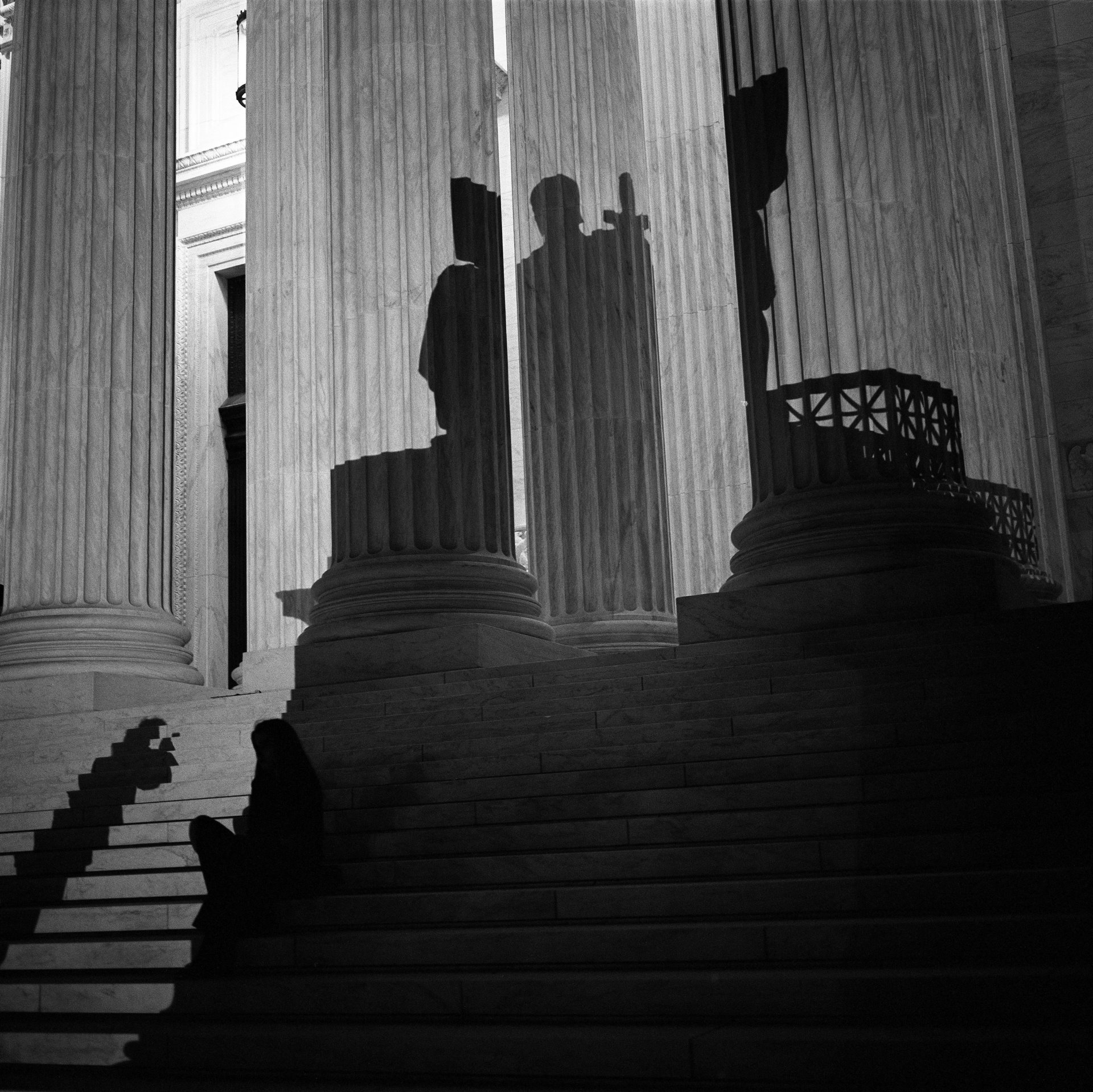 A shadow from the statue known as the Authority of Law is cast by a light used by a television crew onto a woman sitting on the steps of the US Supreme Court, on the night that Supreme Court Justice Ruth Bader Ginsburg died, Washington DC, USA.