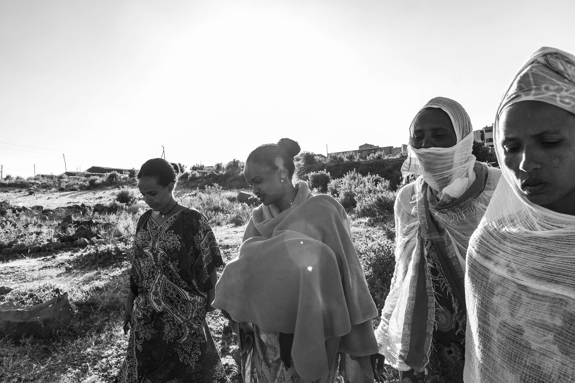 Eritrean women on the outskirts of Addis Ababa, Ethiopia. One of them gave birth a few days ago and is carrying the baby under the blanket. Many Eritrean and Ethiopian women face hardship due to the war, which hinders access to food. In 2020, 8.6 million Ethiopians lacked regular food access, highlighting the impact of conflict on women and their families.