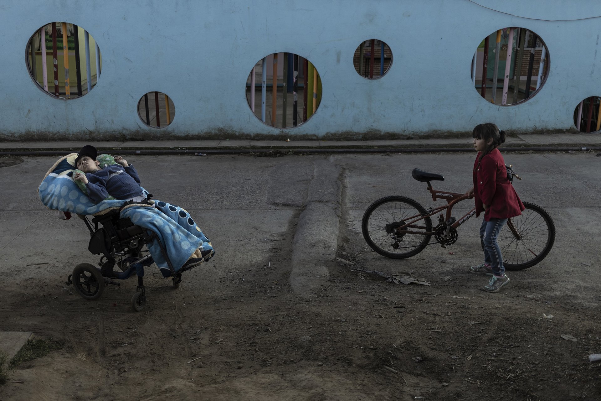 Sebastián (18), who lives with hydrocephalus (a neurological disorder caused by a build-up of fluids in cavities within the brain), waits while his father bunches up flowers to sell in the market, in Villa Guerrero, Mexico. His niece, Valentina, looks on.