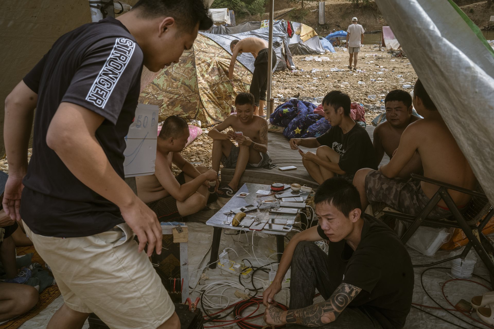 Former workers at the scam center pass time at a makeshift shelter near the Moei River in Min Let Pan, Myanmar. Among the stranded are Chinese nationals reluctant to return to China for fear of prosecution.&nbsp;