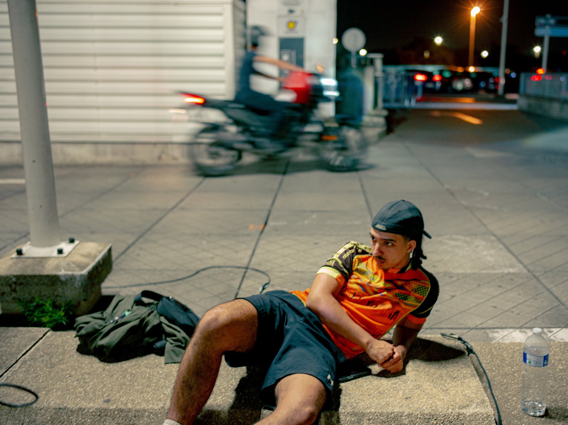 A young man rests amid a gathering on the roof of a parking garage in Aulnay-sous-Bois, France, while others ride their motorcycles.