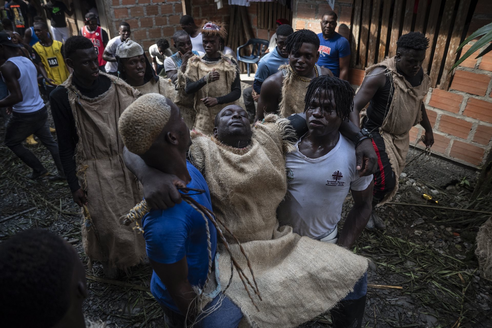 Two people carry an exhausted Manacillo, in Juntas, Buenaventura, Colombia. Tradition dictates that Manacillos cannot sleep for the first 48 hours of the festival; those who fall asleep are ritualistically whipped.&nbsp;
